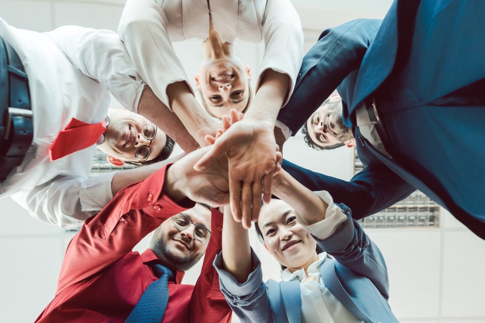 Team of diverse business people stacking their hands together, seen from below - Team of diverse business people stacking their hands together - Team von diversity Geschättsleuten beim Team-building
