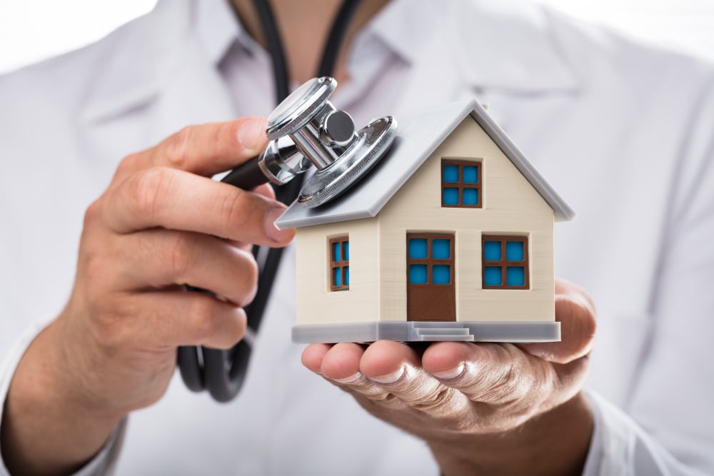 Close-up of a doctor's hand examining house model with stethoscope - Doctor examining house model with stethoscope