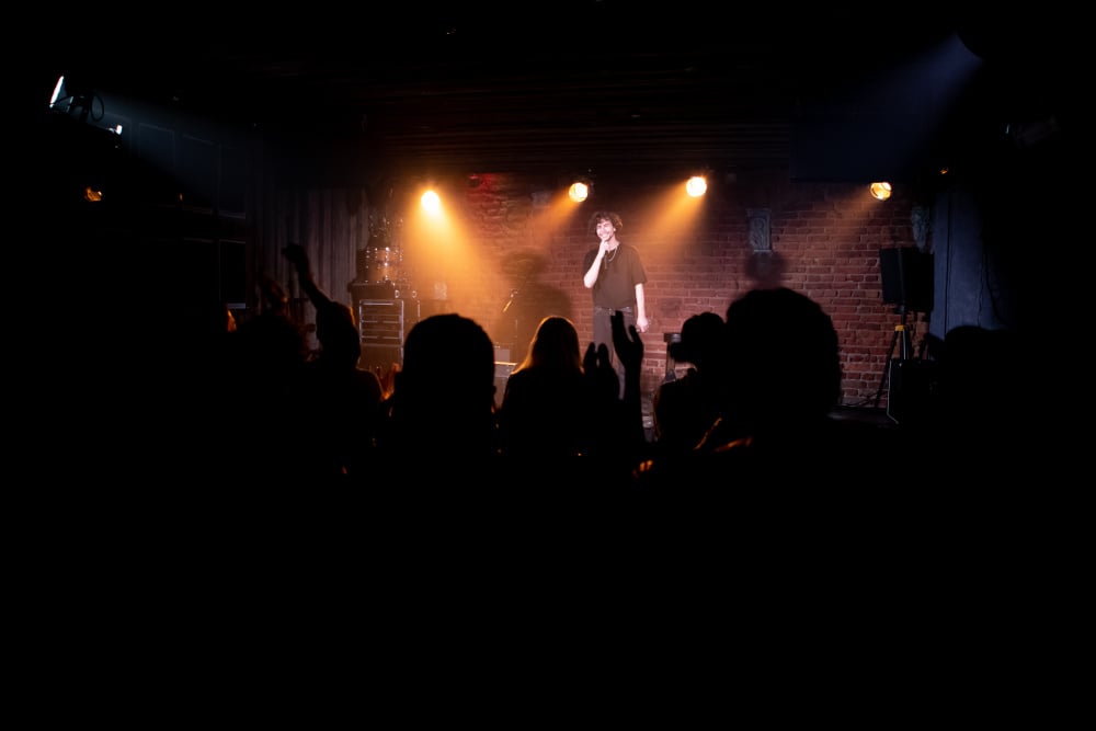 Young Caucasian male comedian performing his stand-up monologue on a stage of a small venue