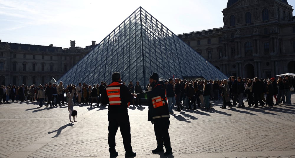 Des visiteurs font la queue devant la pyramide du Louvre.