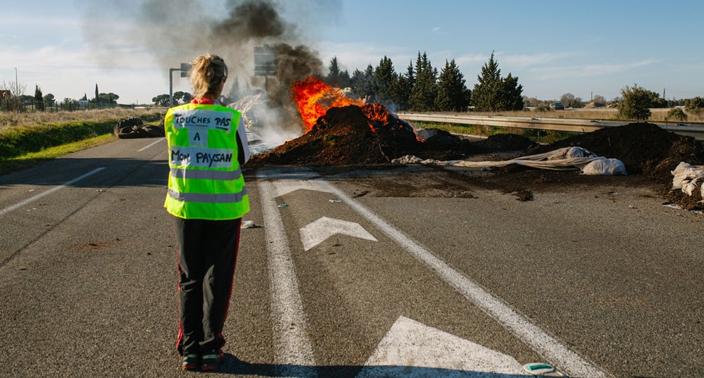 Une manifestante se tient devant des tas d'ordures en feu déposés sur la route lors d'une mobilisation d'agriculteurs à Saint-Martin-de-Crau dans les Bouches-du-Rhône, le 13 décembre 2025.