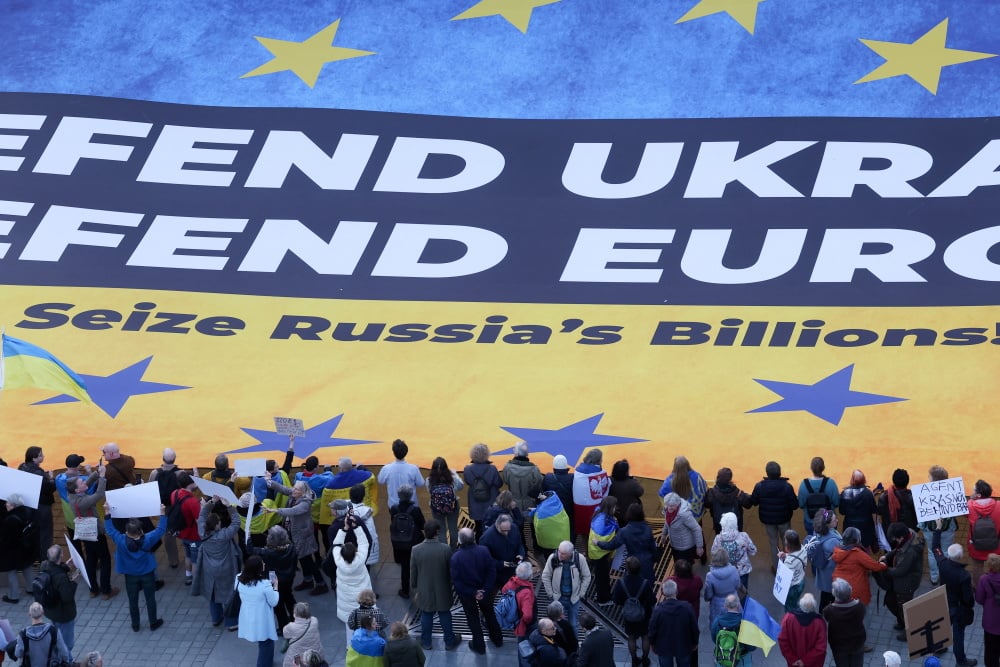 Des militants ukrainiens déploient une immense banderole à Bruxelles, exhortant les dirigeants européens à saisir les avoirs russes gelés afin de financer l’Ukraine dans son conflit contre la Russie, en mars 2025.