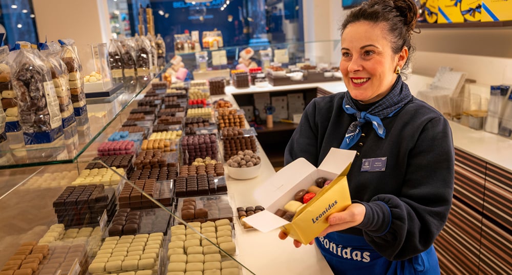 Une vendeuse présente une boîte de chocolats dans une boutique Leonidas.