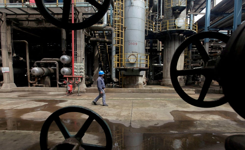 Un ouvrier passe devant des oléoducs dans une raffinerie de Wuhan, en Chine, le 23 mars 2012.