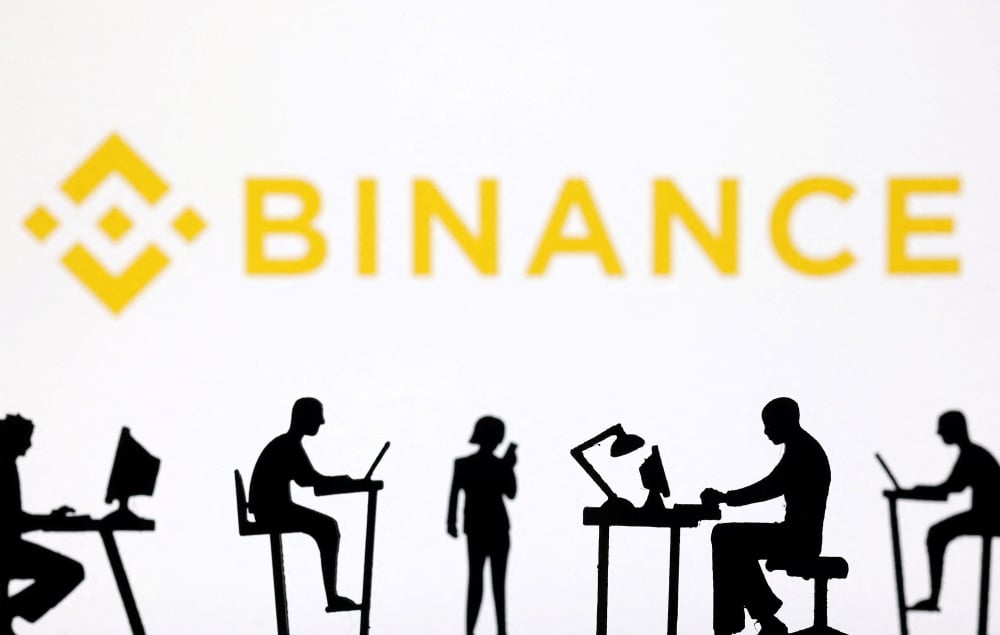 Des figurines d'ordinateurs et de smartphones apparaissent devant le logo de Binance sur cette illustration prise le 19 février 2024.