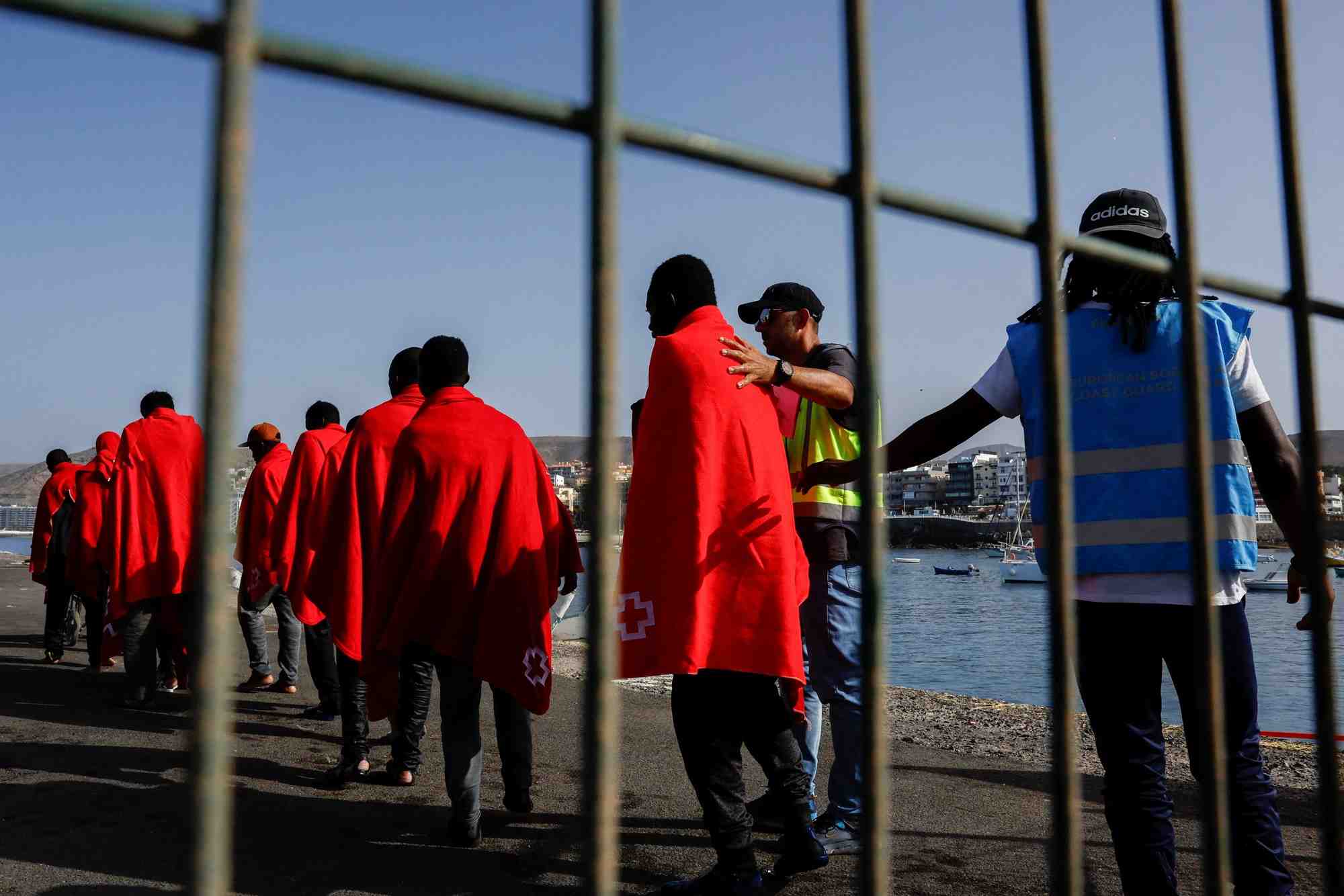 La police frontex accompagne plusieurs migrants vers une tente de la croix-rouge apres leur debarquement d'un navire des garde-cotes espagnols, dans le port d'arguineguin
