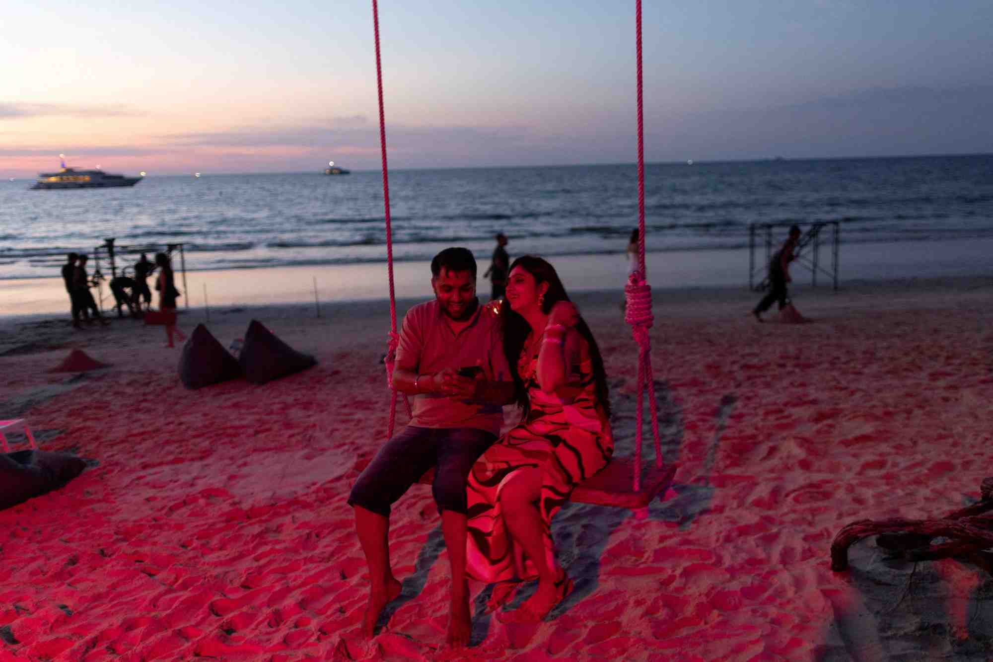 Un couple est assis sur une balancoire au crepuscule sur une plage de phuket
