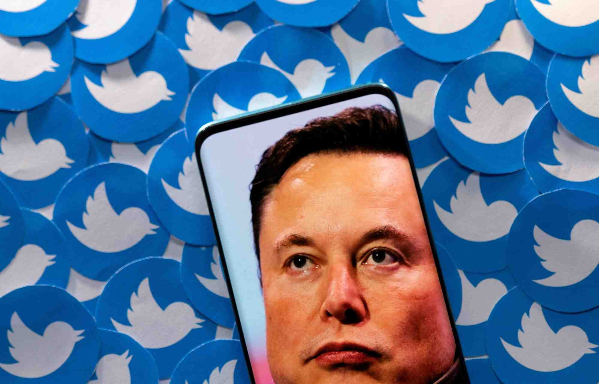 Une illustration montre l'image d'elon musk sur un smartphone et des logos twitter imprimes