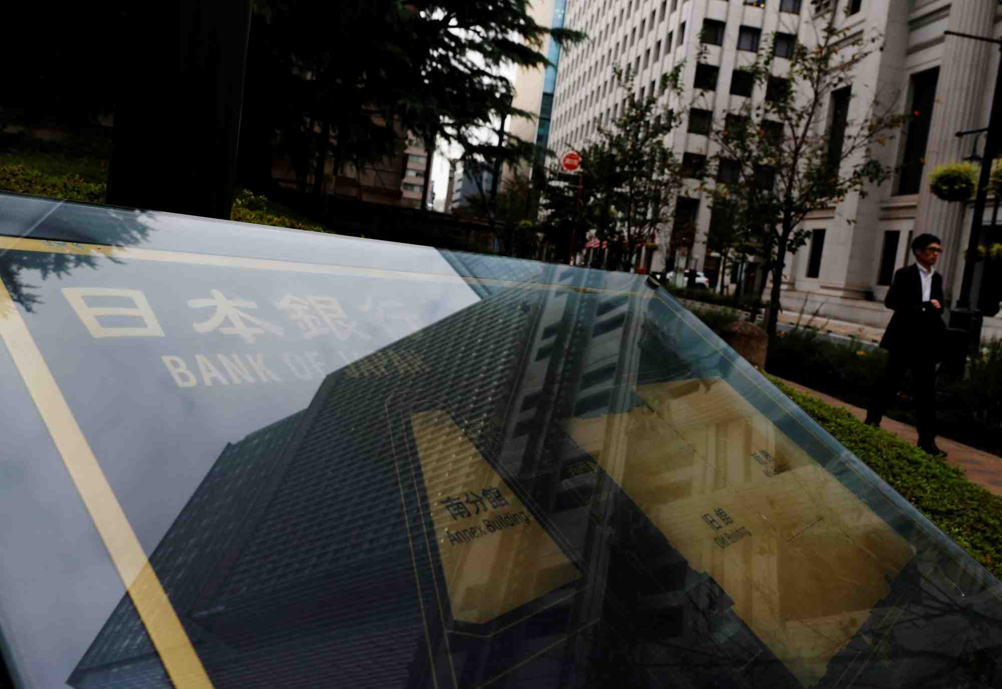 Photo d'un homme qui passe devant une pancarte de la banque du japon devant son siege a tokyo