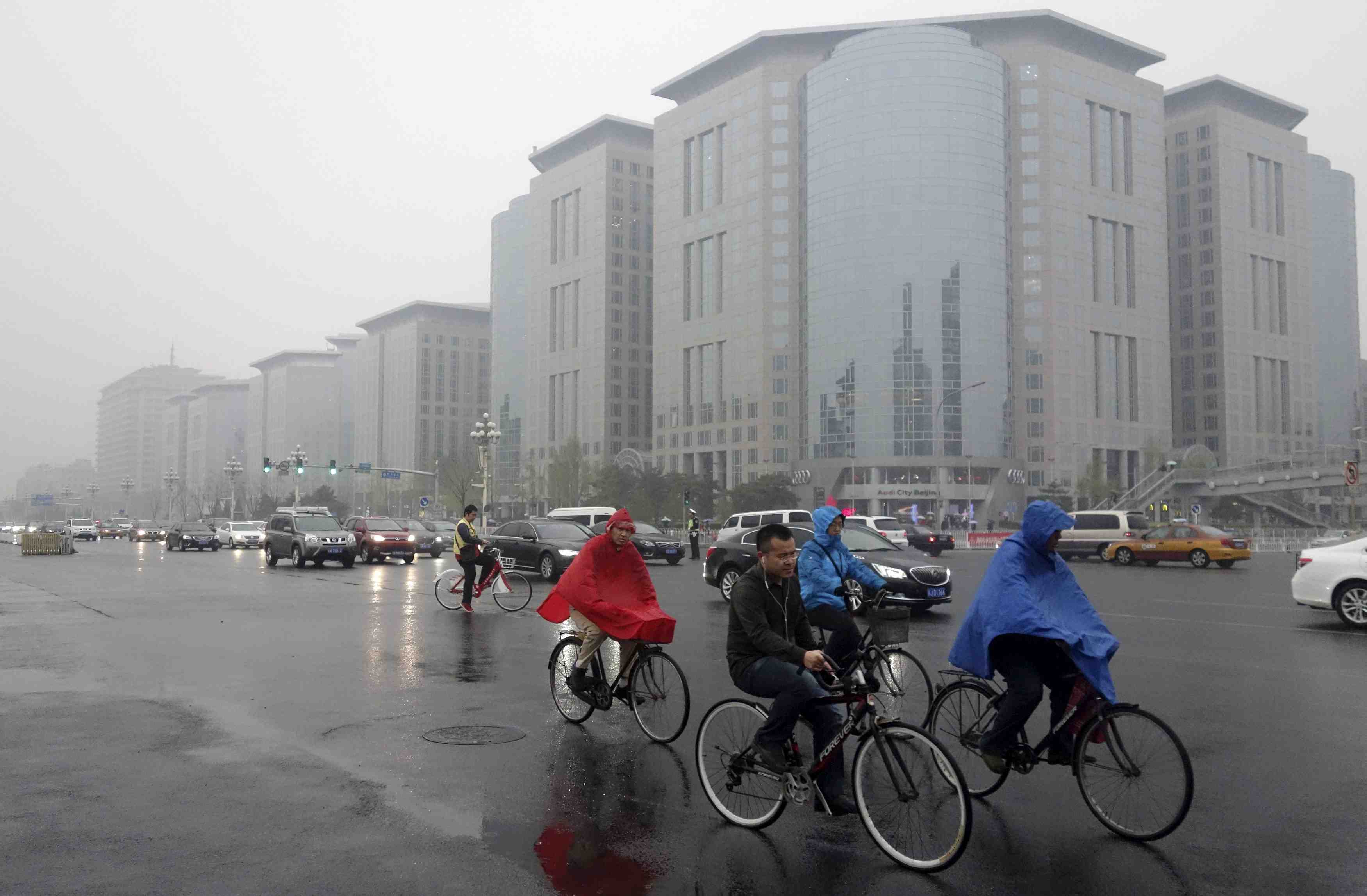 Residents ride their bicycles next to vehicles traveling along the chang'an avenue amid rainfalls on a hazy day in central beijing