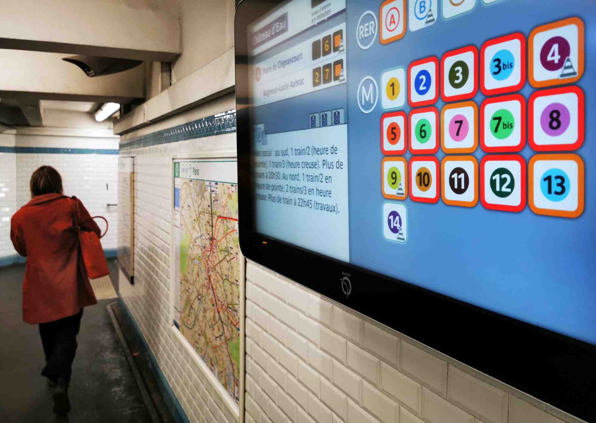 Une femme passe devant un ecran d'information affichant la liste des lignes de metro dont le service est interrompu a paris