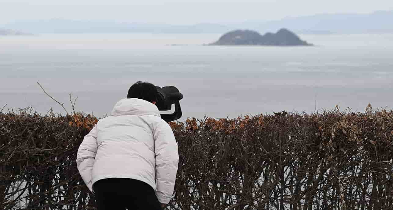 Un homme observe la côte nord-coréenne avec des jumelles depuis l'île sud-coréenne de Yeonpyeong, près de la frontière maritime nord-coréenne, le 8 janvier 2024.