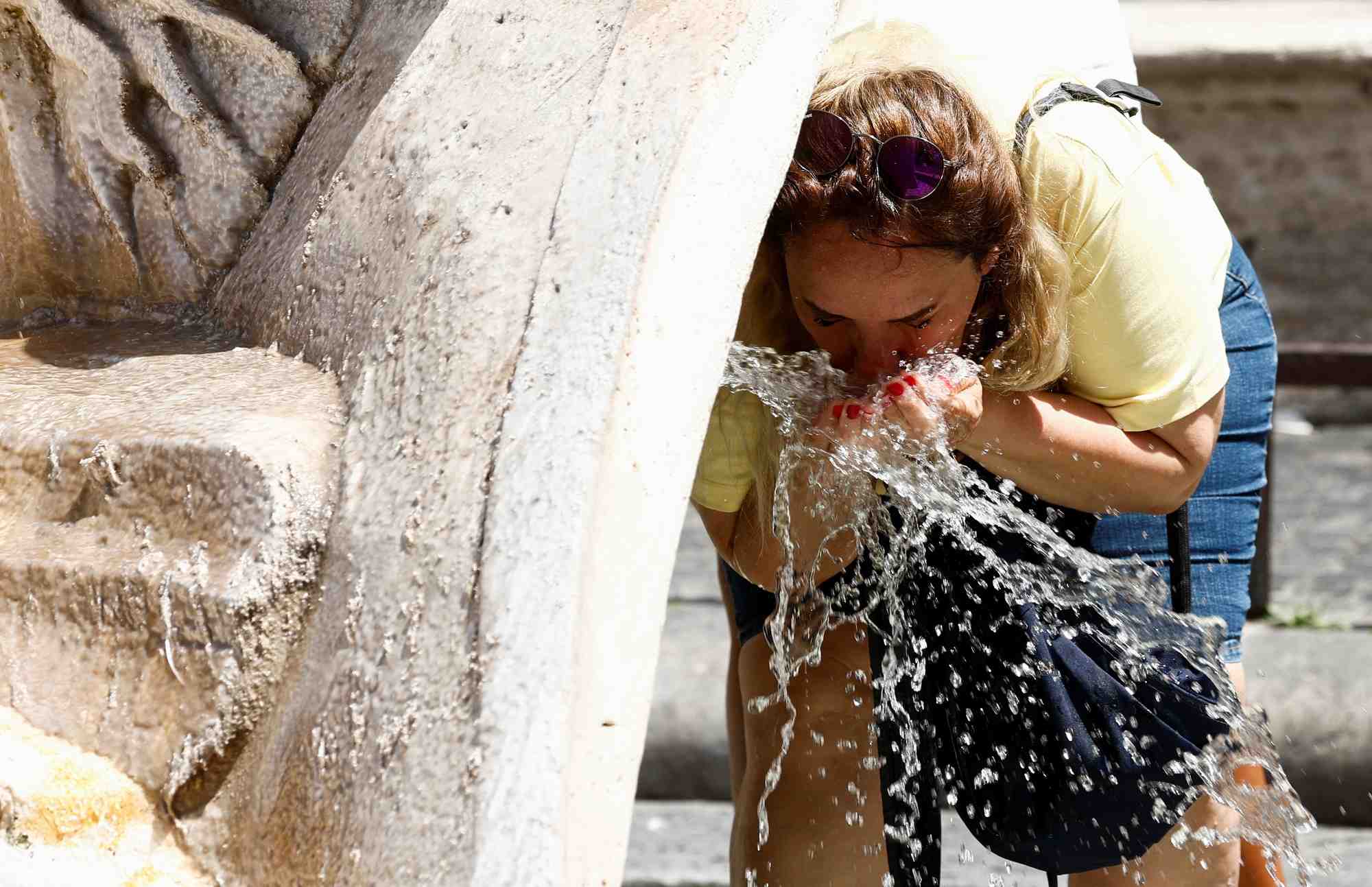 Une personne se rafraichit a la fontana della barcaccia pendant une canicule a rome