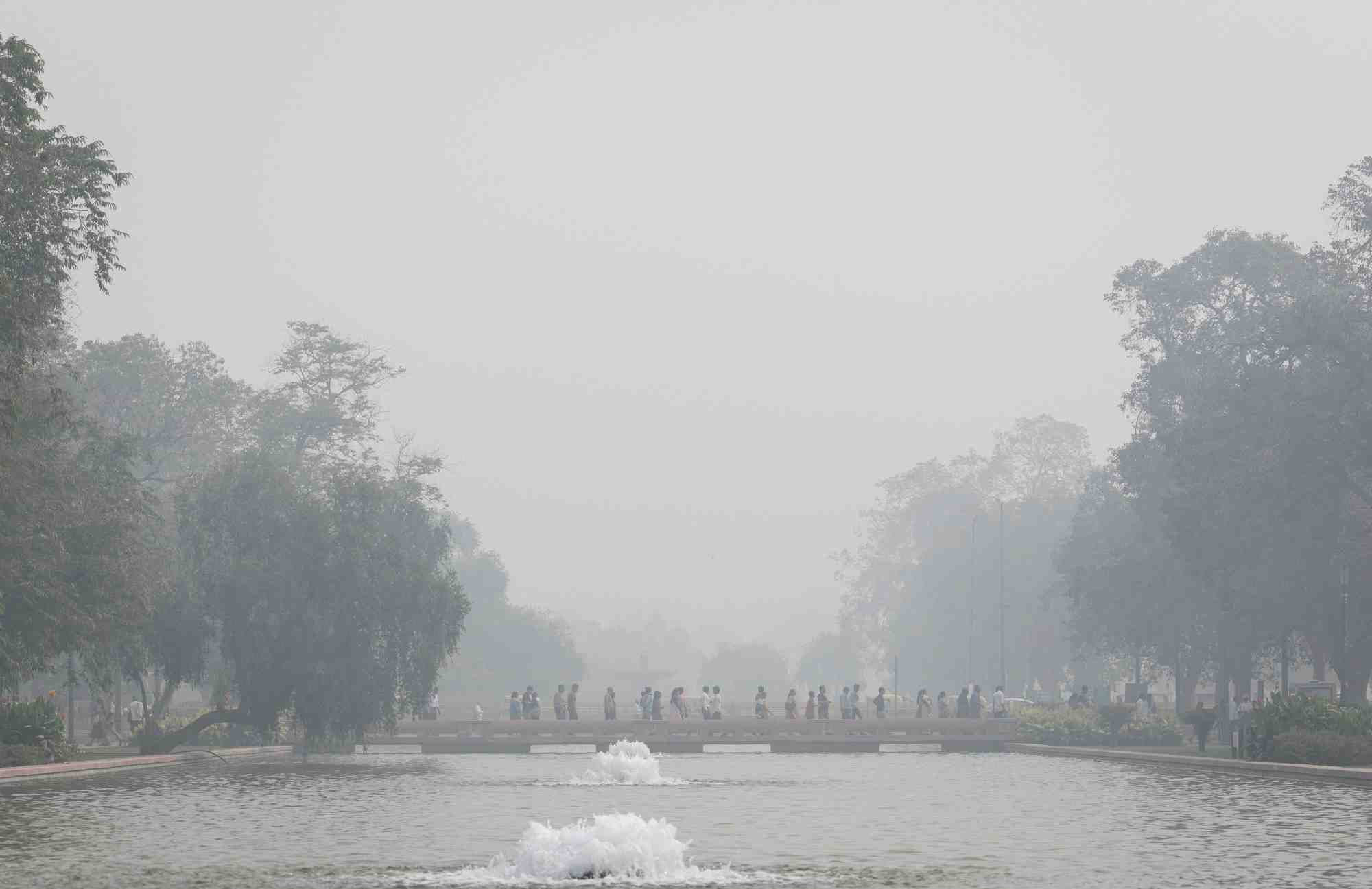 Des personnes marchent sur un sentier au-dessus d'un etang au milieu d'un lourd smog a new delhi