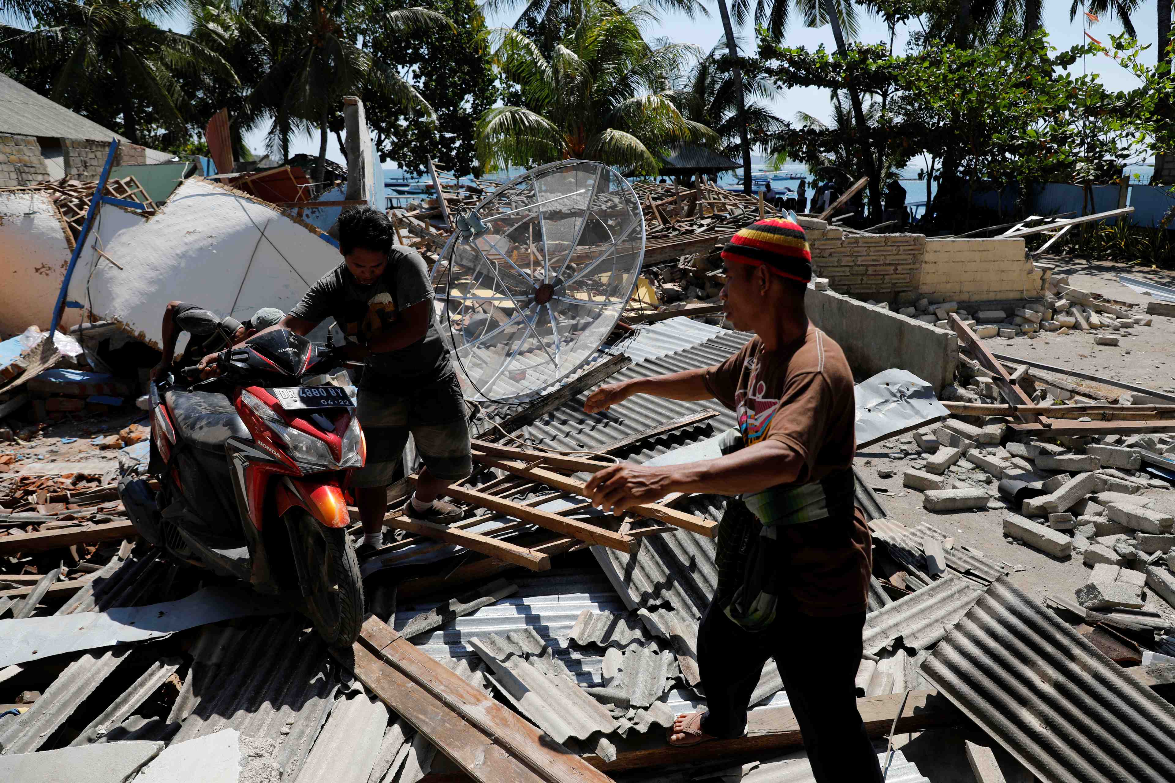 Villagers push a motorcycle on debris after an earthquake hit lombok island in pemenang
