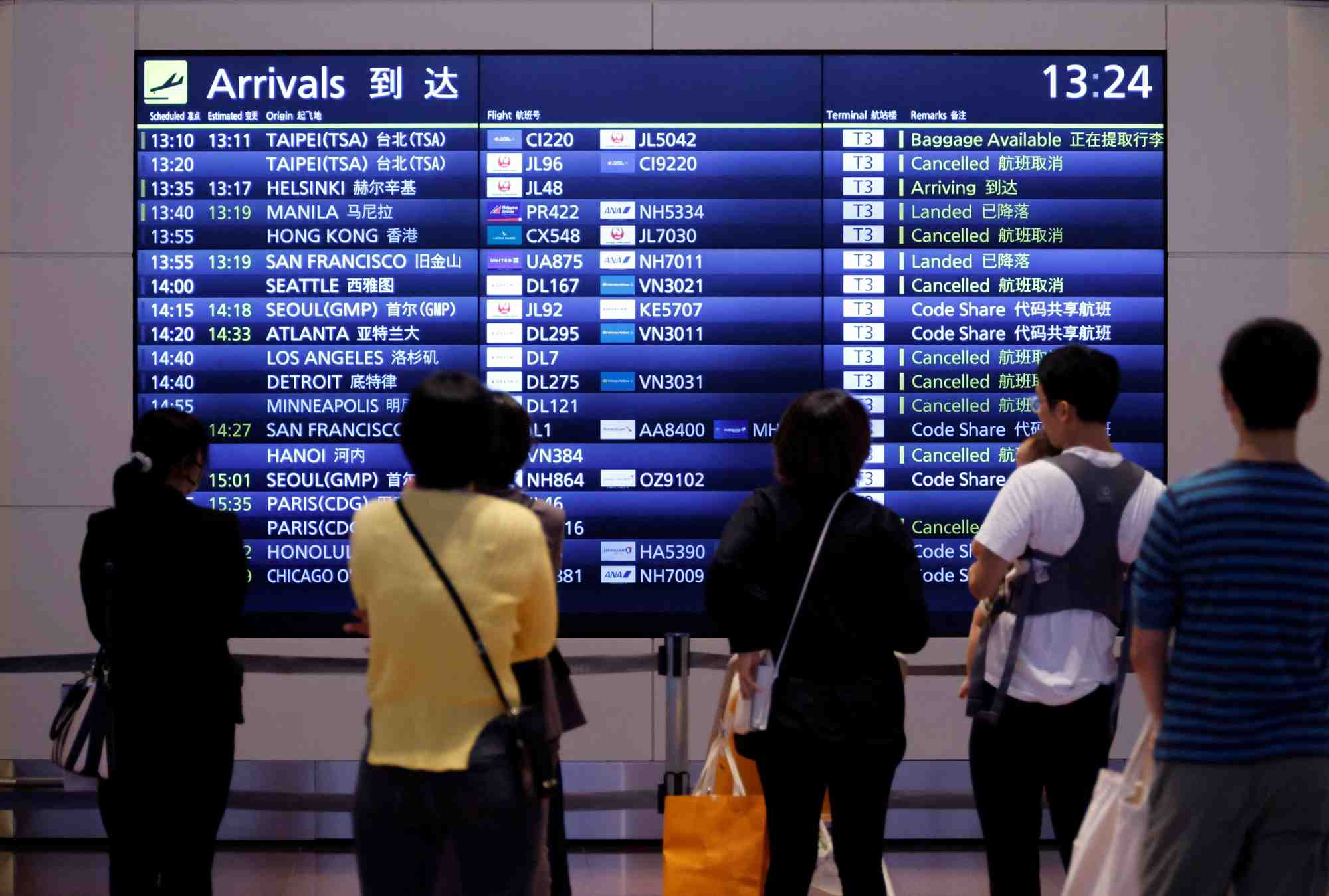 Des personnes devant un panneau d'information sur les vols a l'aeroport international de haneda, a tokyo
