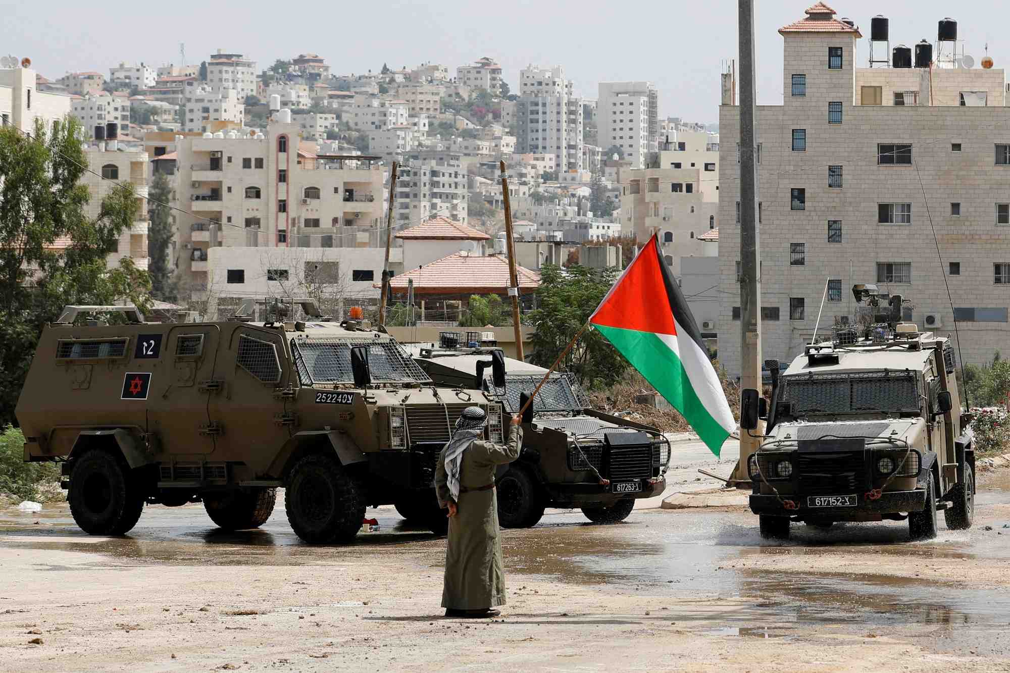 Un homme tient un drapeau palestinien a cote de vehicules militaires israeliens
