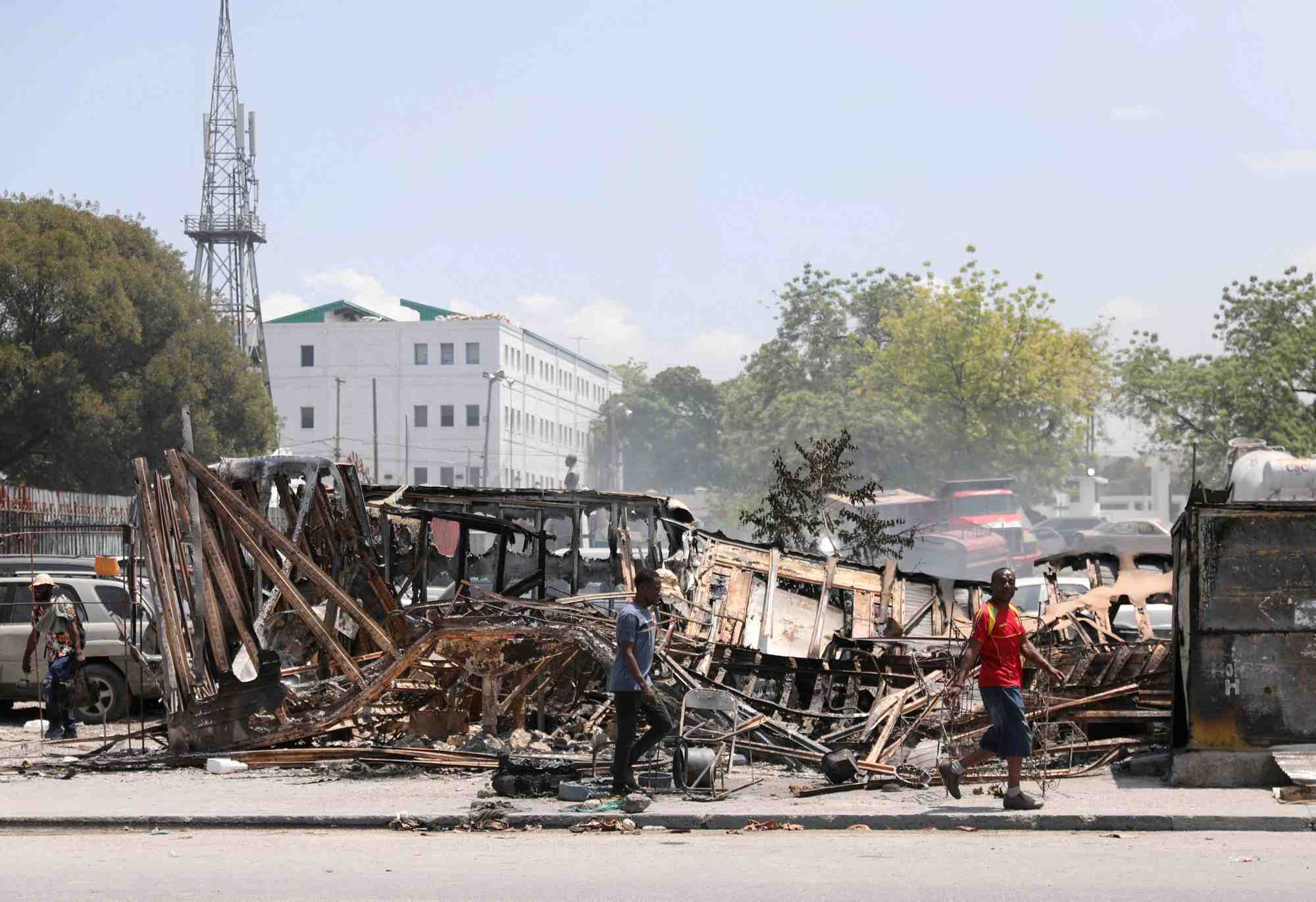 Des gens passent devant les restes de vehicules incendies par des gangs, a port-au-prince