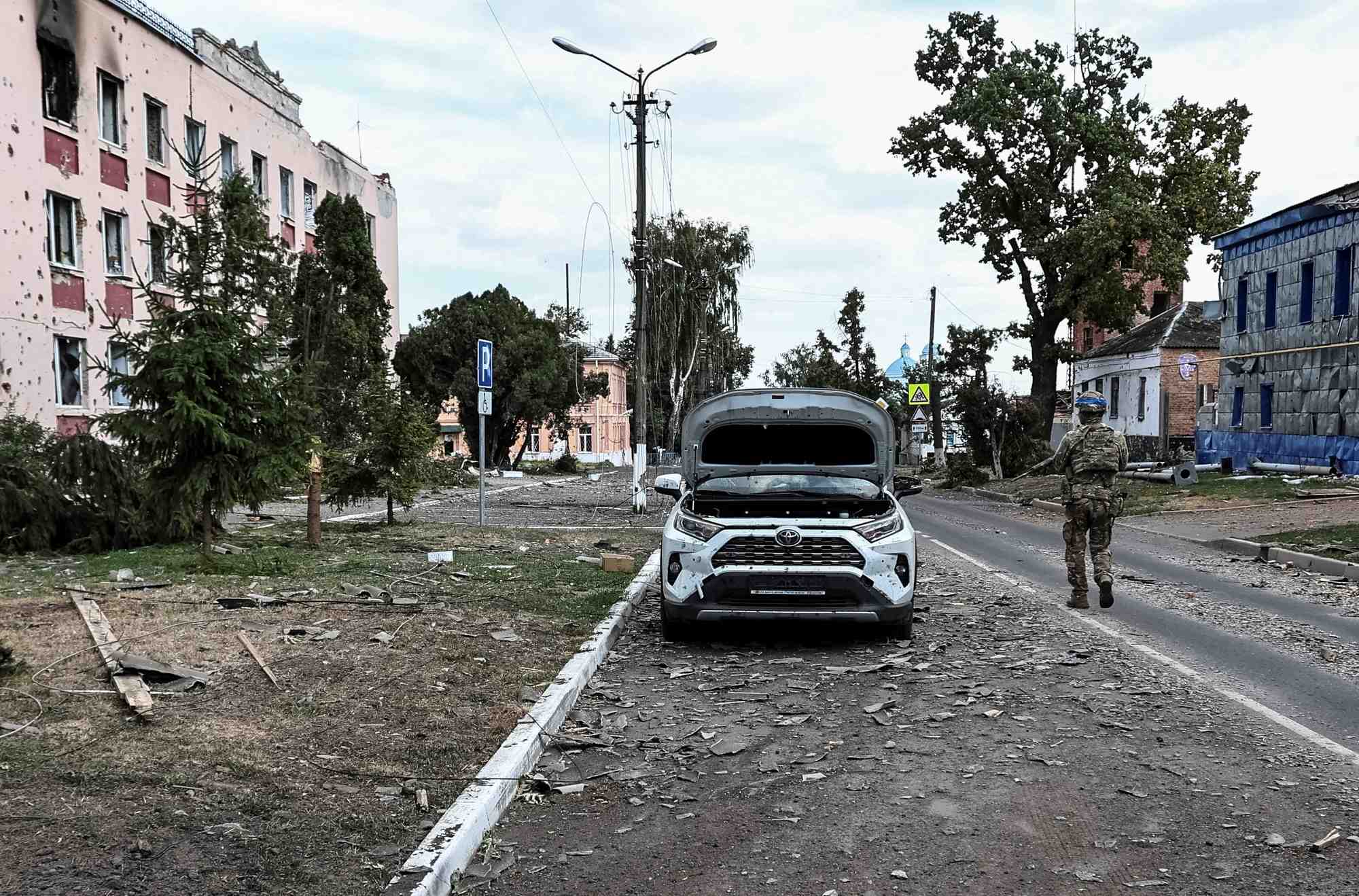 A ukrainian serviceman patrols a street next to damaged buildings in the town of sudzha