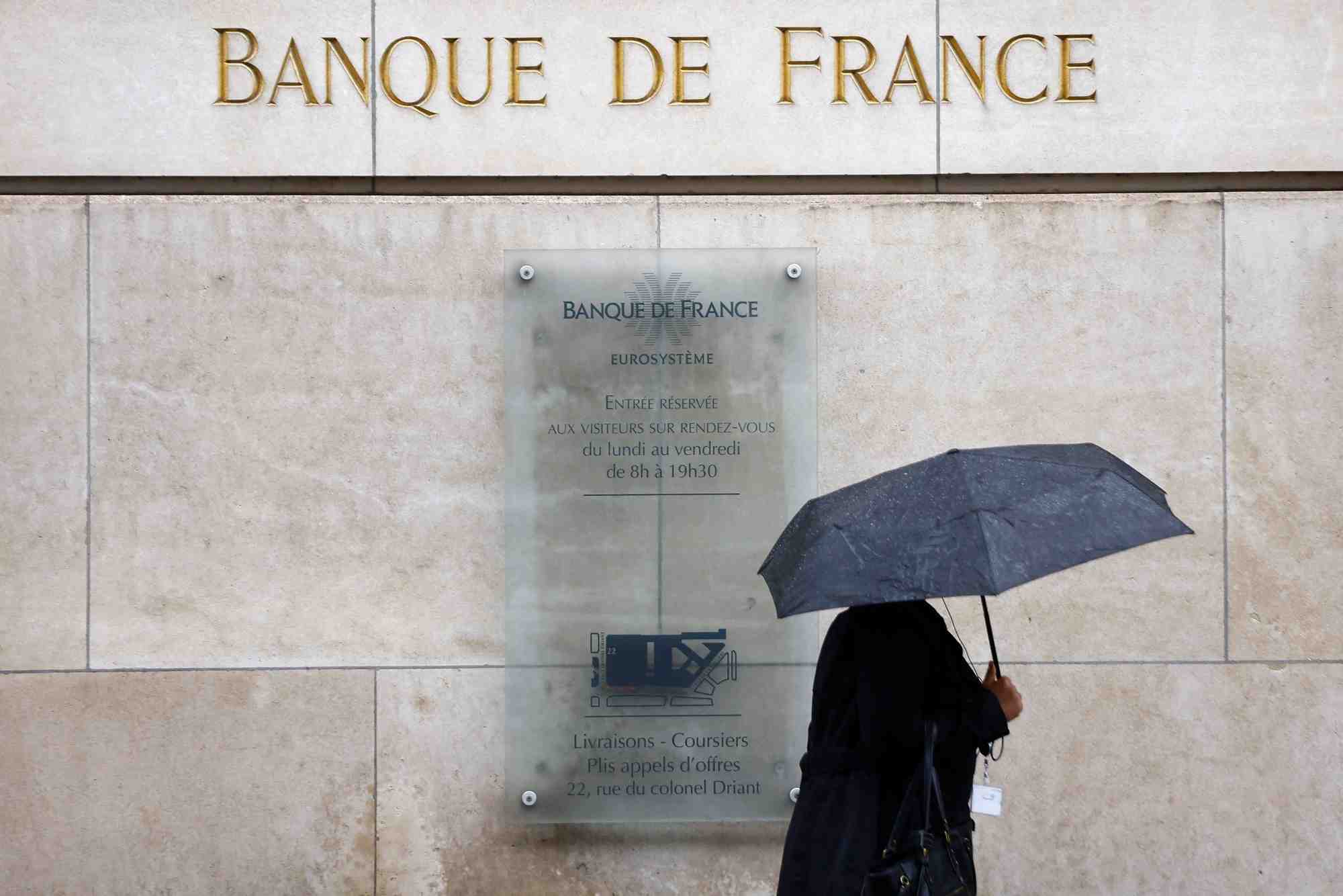 Une femme tenant un parapluie passe devant le batiment de la banque de france a paris
