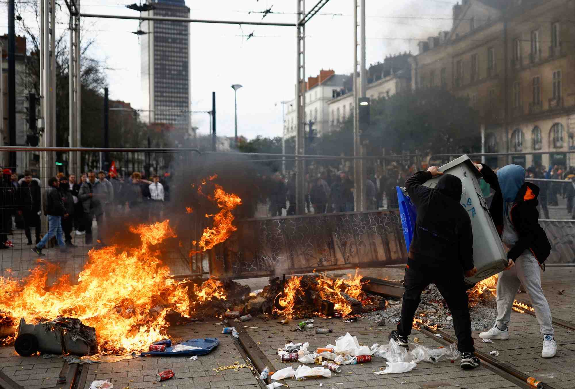 Photo des gens qui portent une poubelle a cote d'un incendie lors d'affrontements pendant une manifestation pour protester contre l'article 49.3 de la constitution