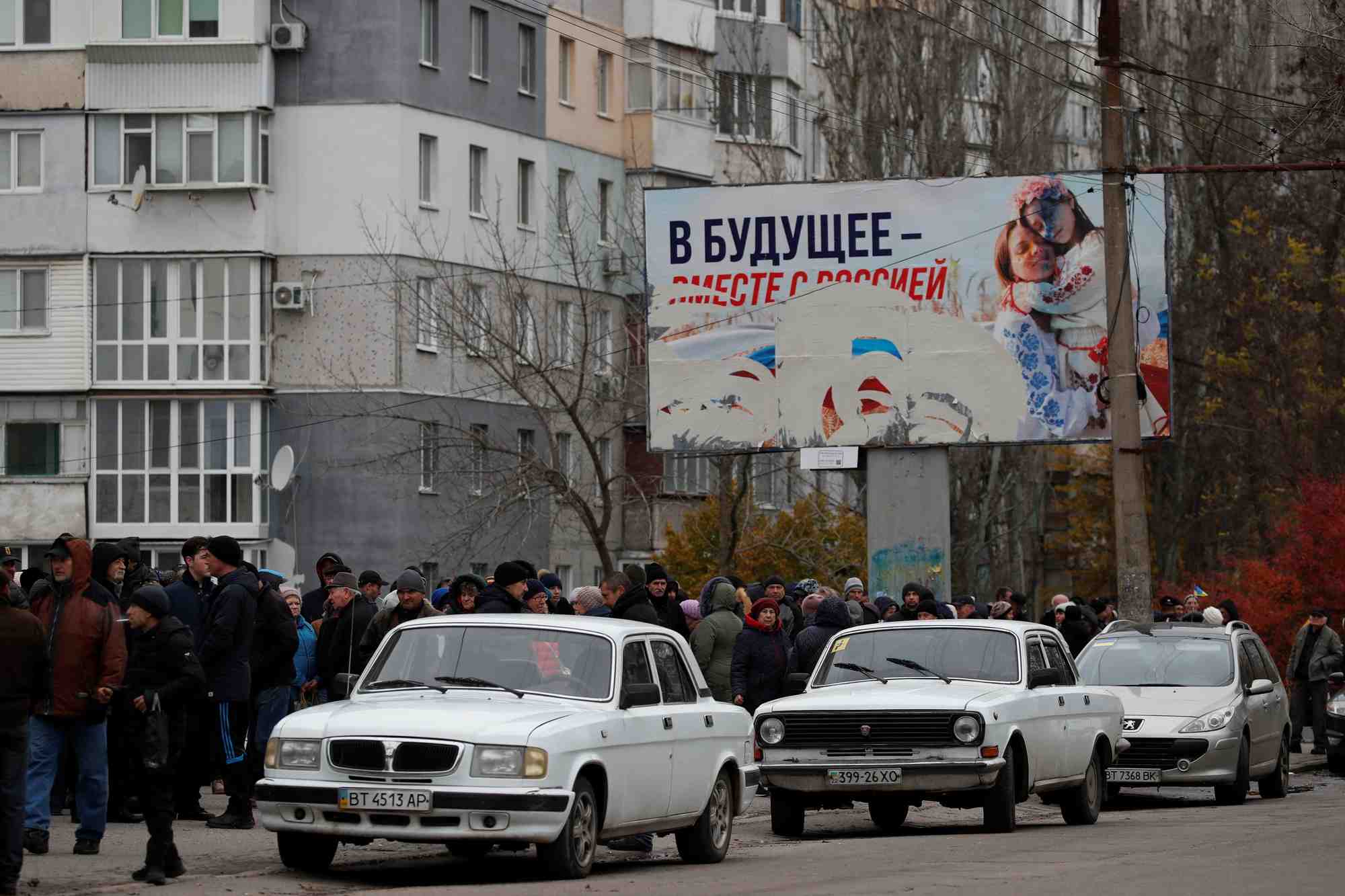 Des personnes attendent la distribution d'aide humanitaire, avec un panneau publicitaire pro-russe en arriere-plan, a kherson