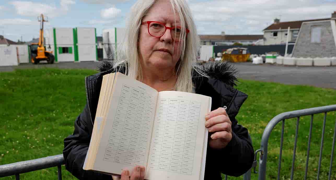 Anna Corrigan, 69 ans, dont les deux frères seraient morts à Thuam, montre un registre des victimes.