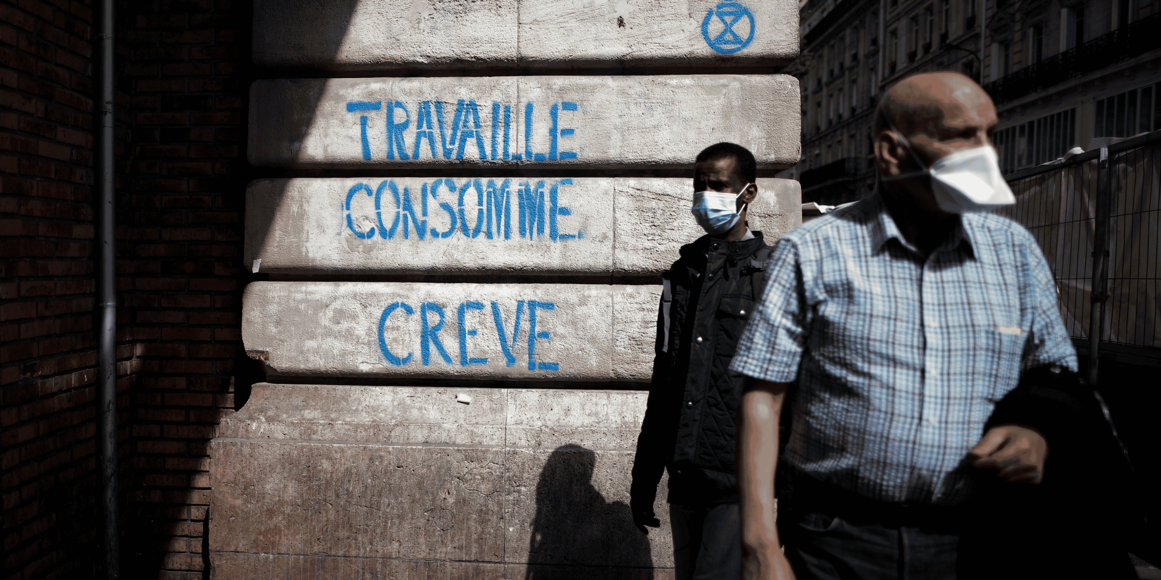 Coronavirus : deux personnes portant un masque passent devant un slogan disant : "Travaille, consomme, crève" (à Paris)