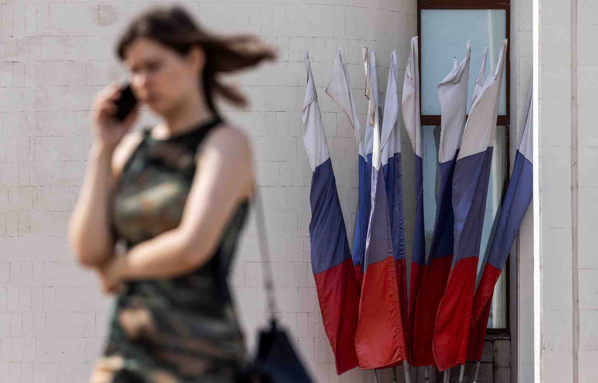 Une femme parle au telephone en passant devant des drapeaux nationaux russes a koursk