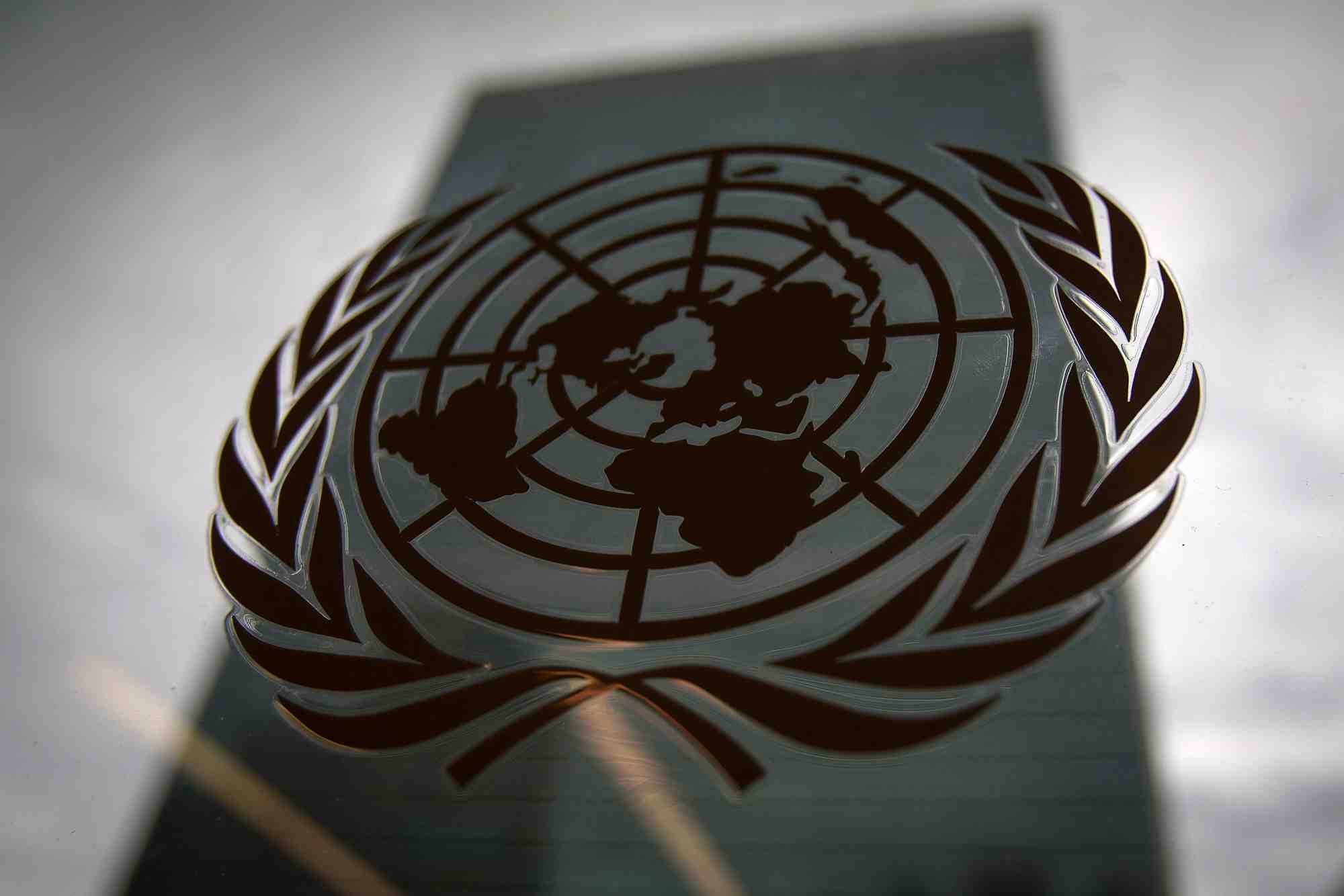Le batiment du siege des nations unies se reflete dans une fenetre avec le logo de l'onu au premier plan, new york