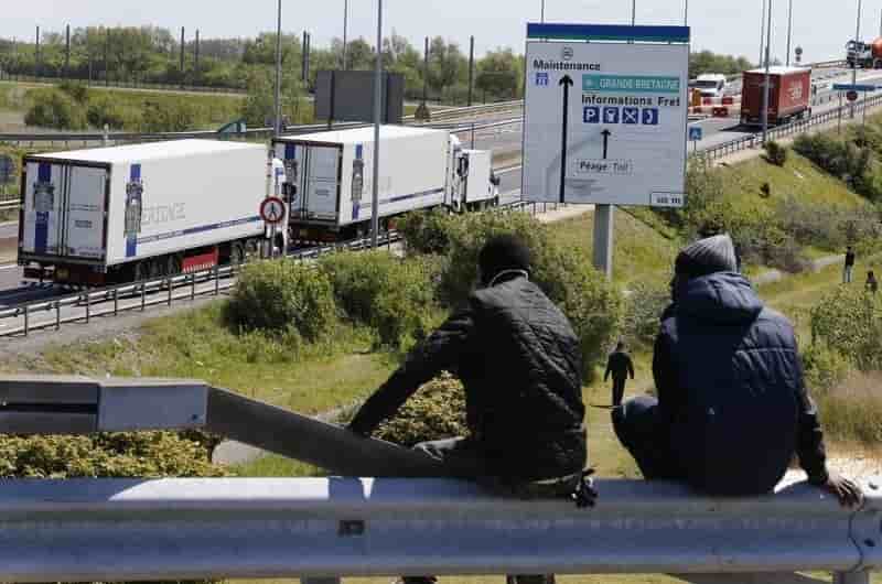 Two migrants sit on a guardrail which overlooks the road that lorries take to reach the channel tunnel crossing in calais