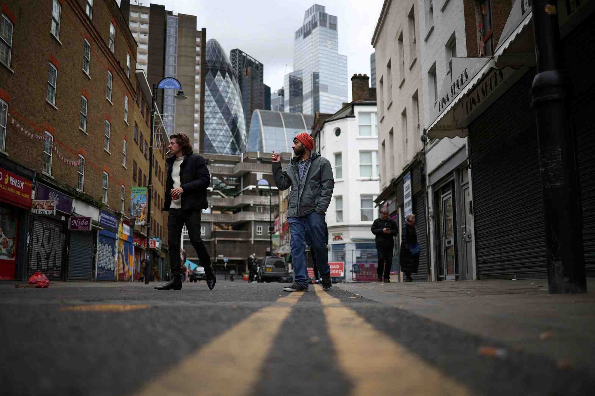 Des personnes passent devant des magasins, avec le quartier financier de la city de londres en arriere-plan