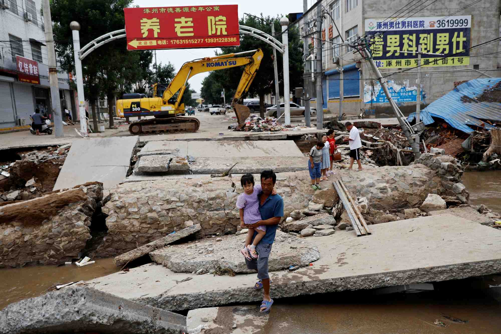 Photo d'archives qui montre un homme tenant un enfant et traversant un pont endommage apres les pluies et les inondations provoquees par les restes du typhon doksuri