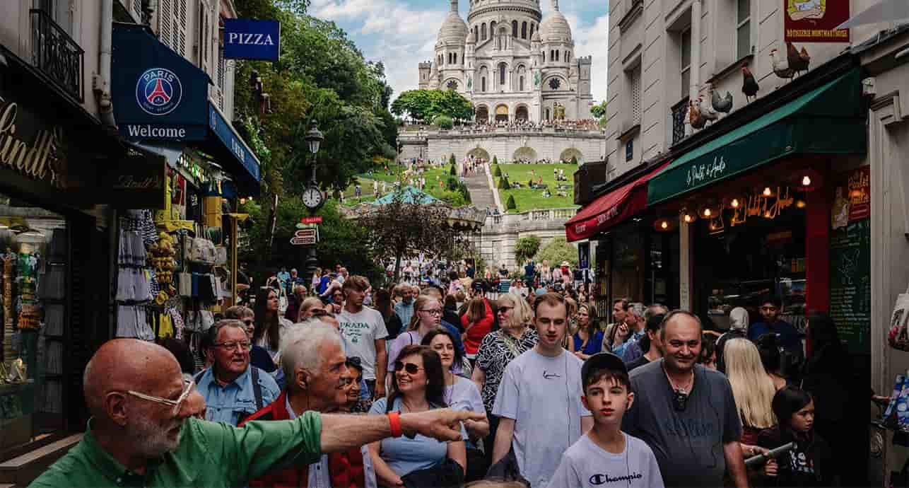 Des touristes se promènent le long de la rue Steinkerque avec la basilique du Sacré-Cœur sur la butte Montmartre en arrière-plan, à Paris, le 1er août 2025.