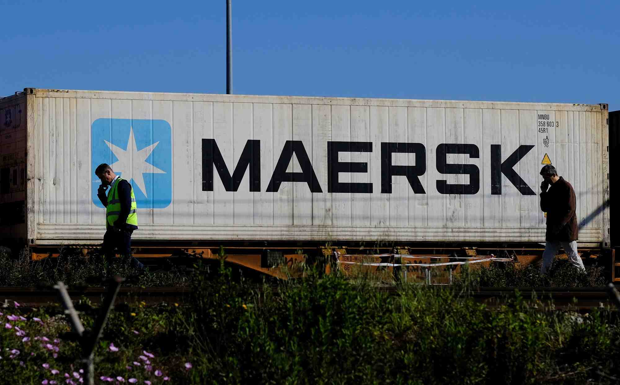 Des travailleurs parlent sur leur telephones portables, alors qu'un conteneur maersk est transporte par un train, pres du port de barcelone