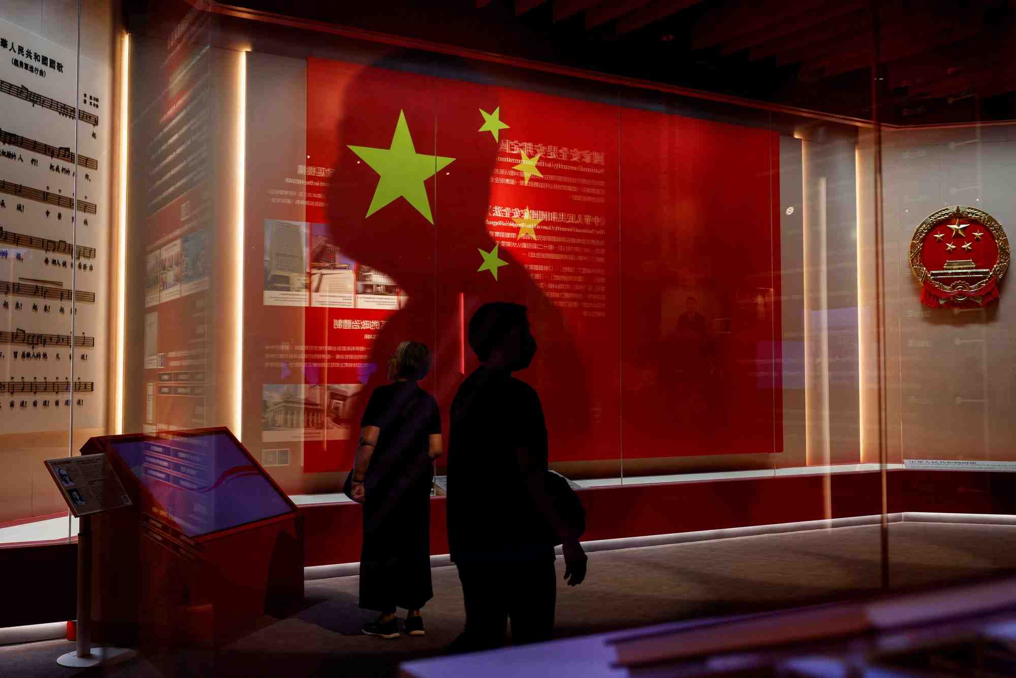 Des visiteurs passent devant le drapeau national chinois et l'embleme a la galerie d'exposition de la securite nationale, avant le 75e jour national de la chine a hong kong