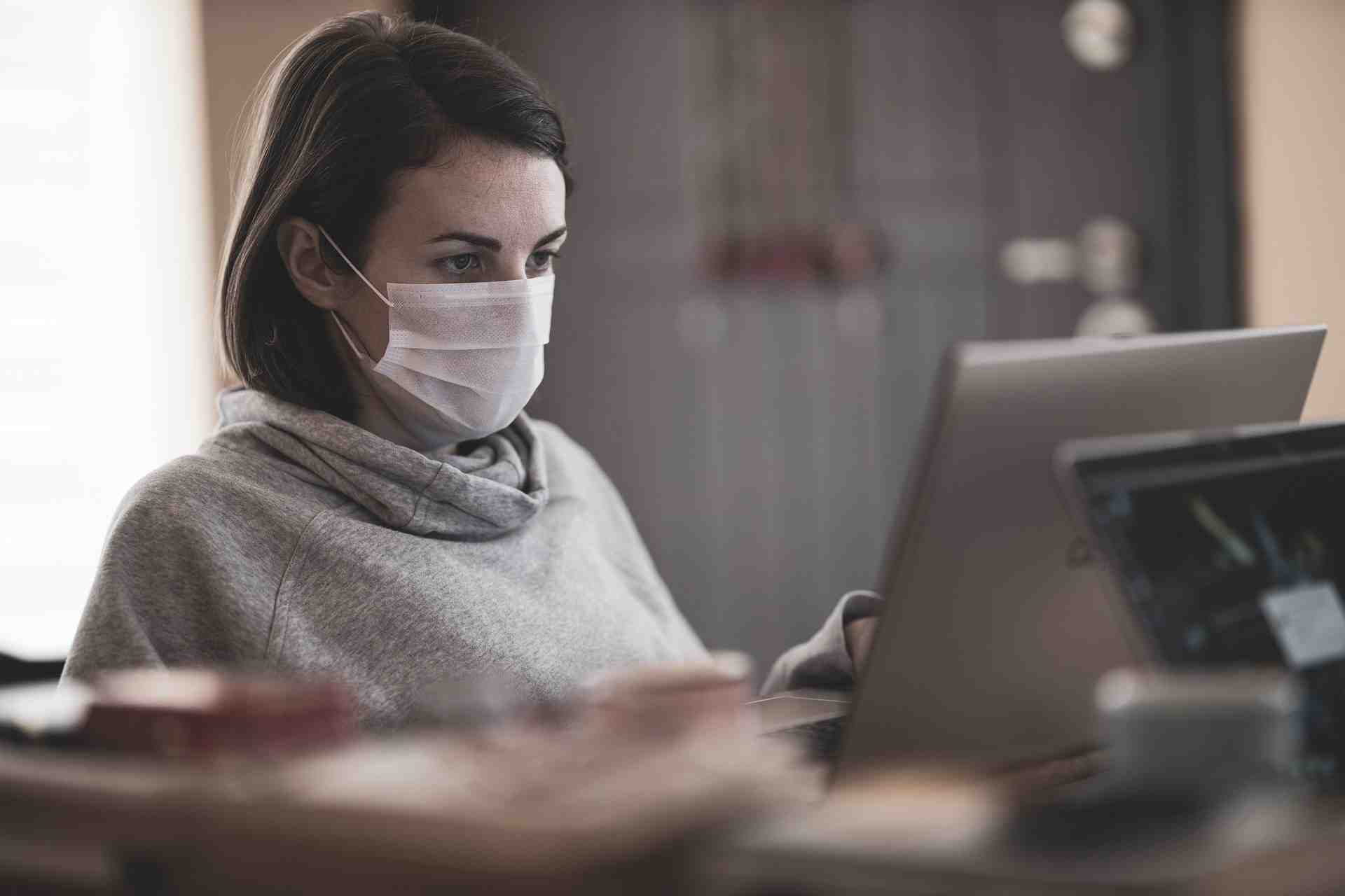 Femme avec un masque devant son ordinateur