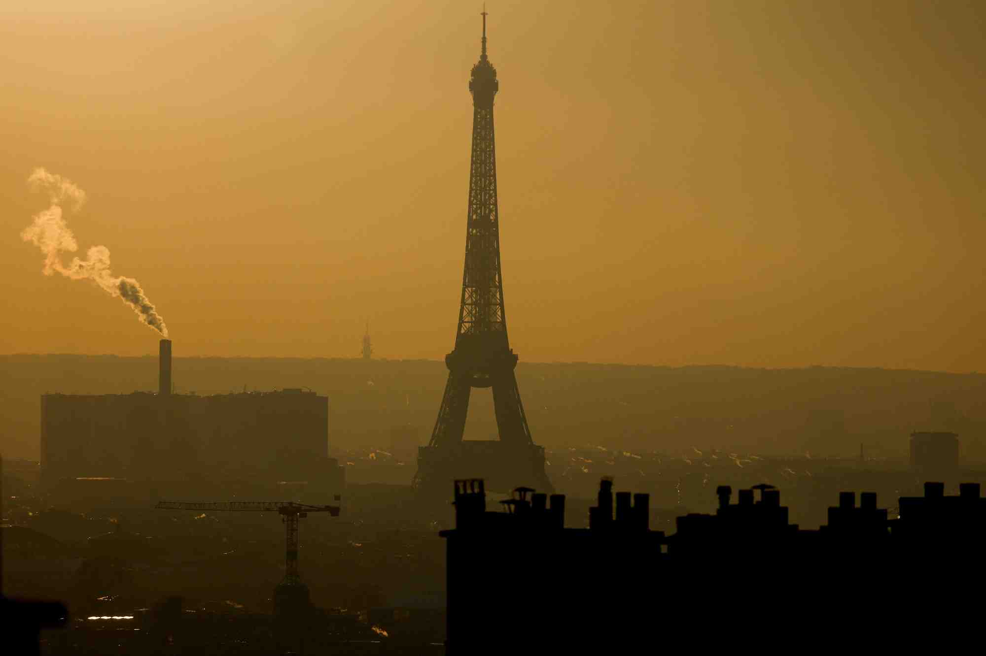 Une vue d'ensemble montre la tour eiffel et la vapeur qui s'echappe des cheminees dans l'horizon de paris