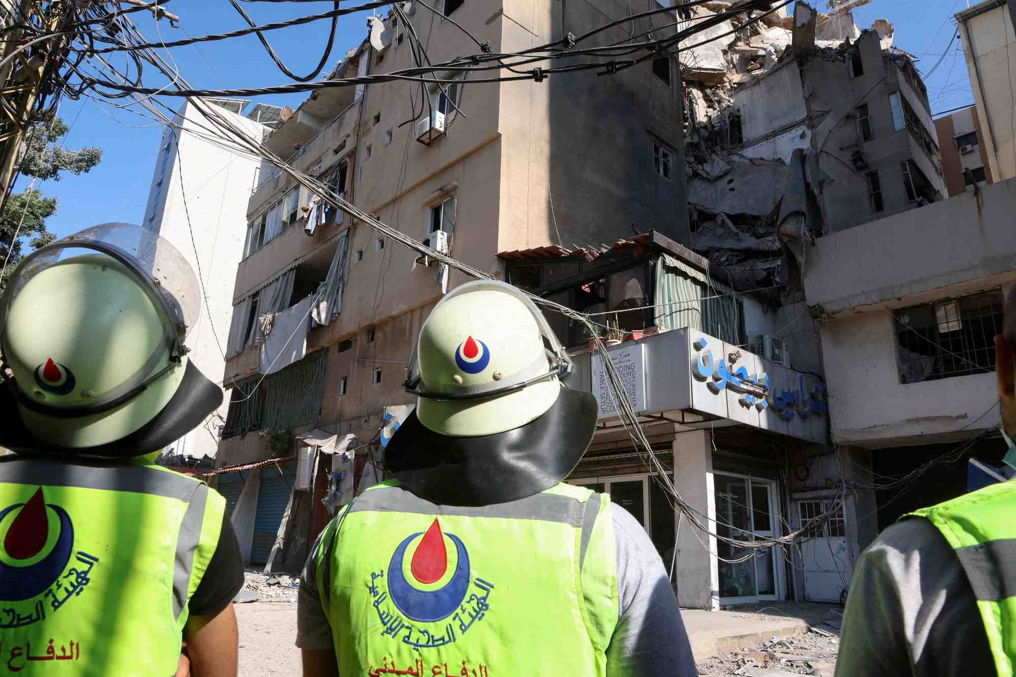 Des membres de la defense civile se tiennent pres d'un batiment endommage au lendemain d'une frappe israelienne a beyrouth