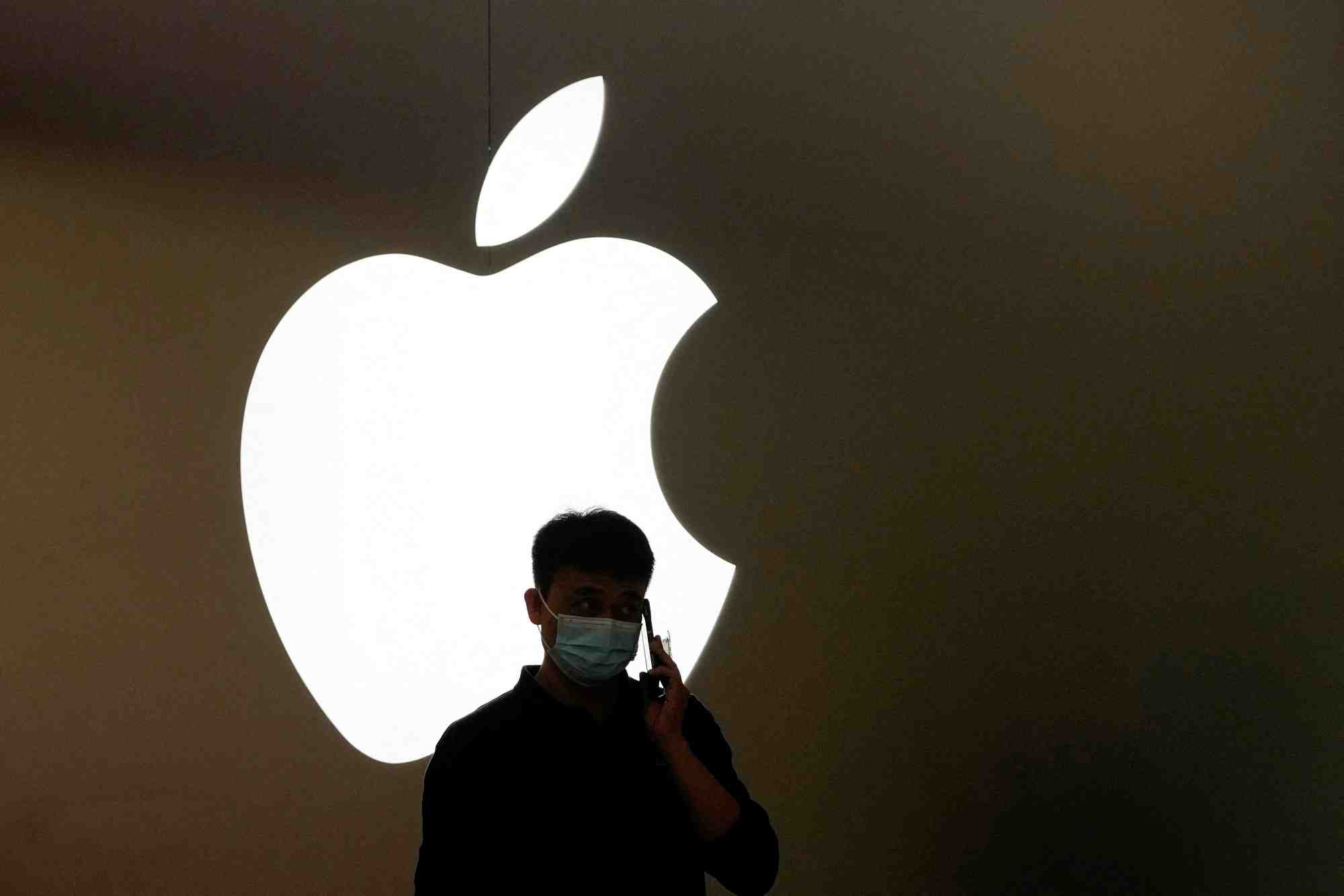 Un homme parle au telephone devant le logo d'apple a l'exterieur d'un magasin a shanghai