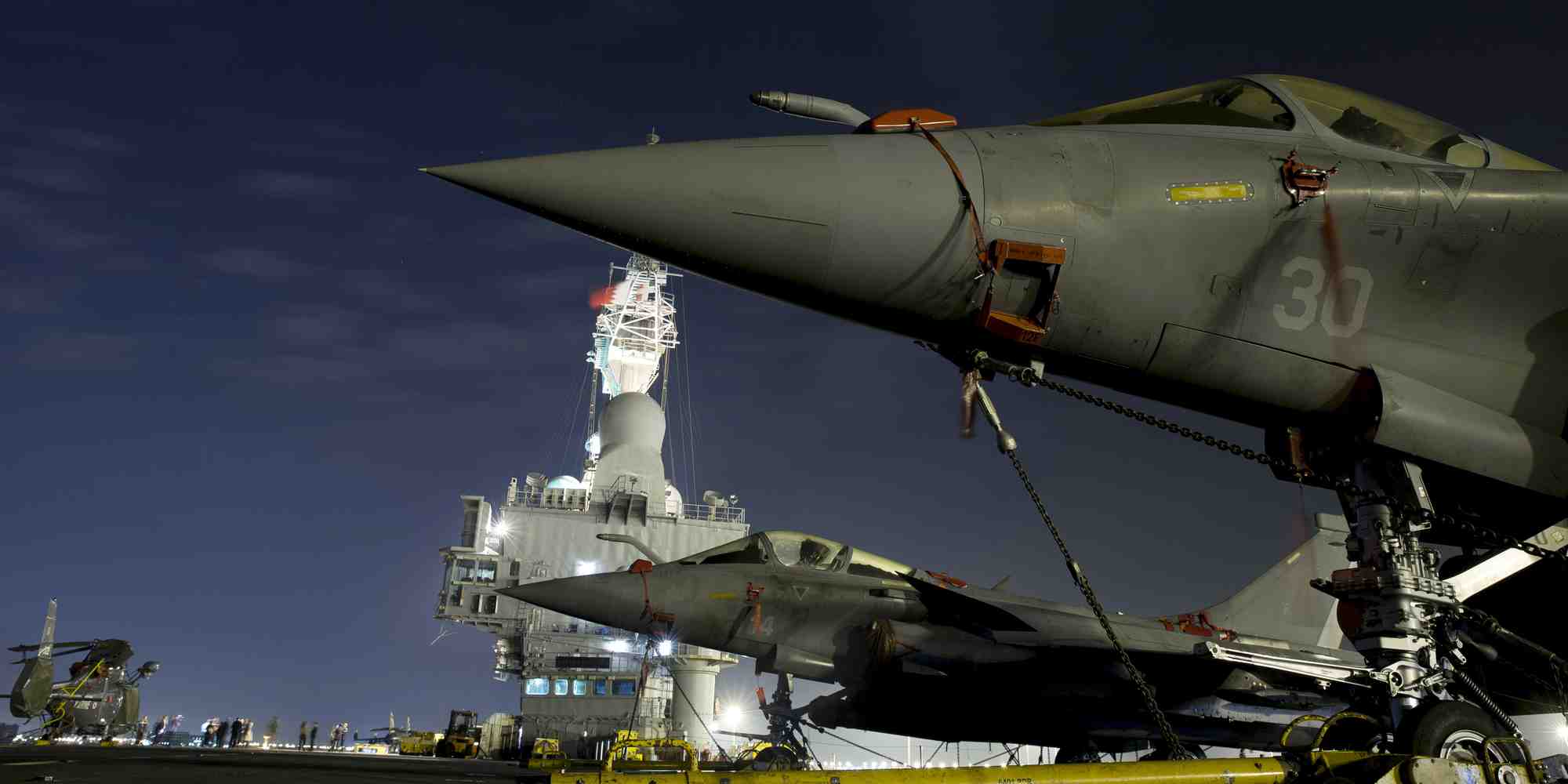 Un porte-avions est un navire de guerre et, s'il peut remplir des missions diplomatiques de présence, il faut, pour que celles-ci soient crédibles, qu'il soit aussi capable d'intervenir militairement, qu'il sache effectivement combattre. (Illustration: photo du porte-avions nucléaire "Charles-de-Gaulle" prise depuis le pont d'envol avec, au premier plan, sur le côté de la piste d'envol oblique, deux chasseurs Rafale stationnés, petite partie du groupe aéronaval embarqué.)