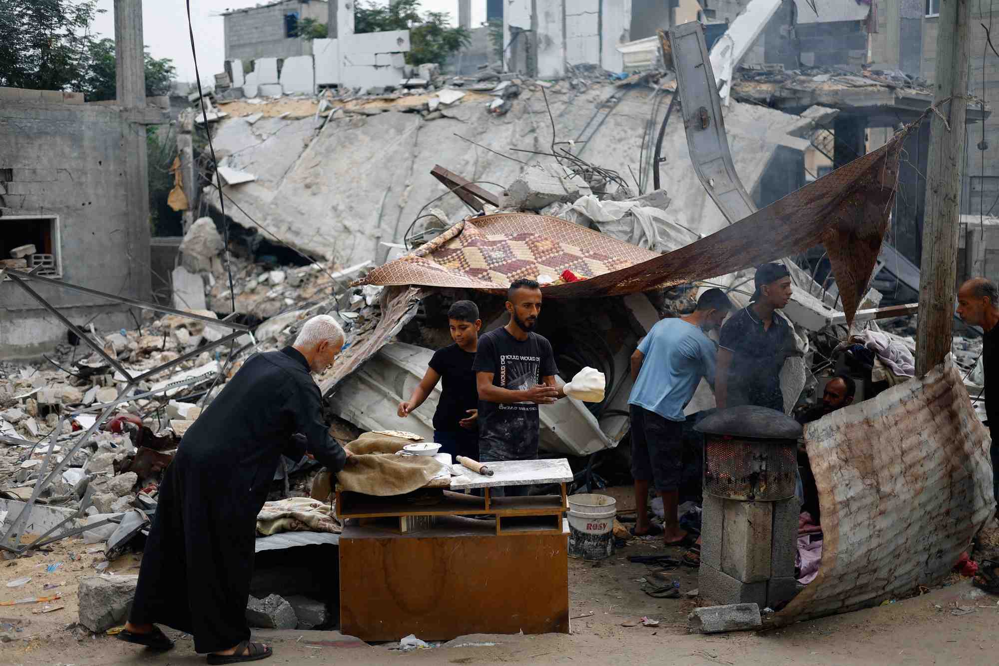 Des palestiniens preparent de la nourriture a cote des debris causes par des frappes israeliennes dans le sud de gaza