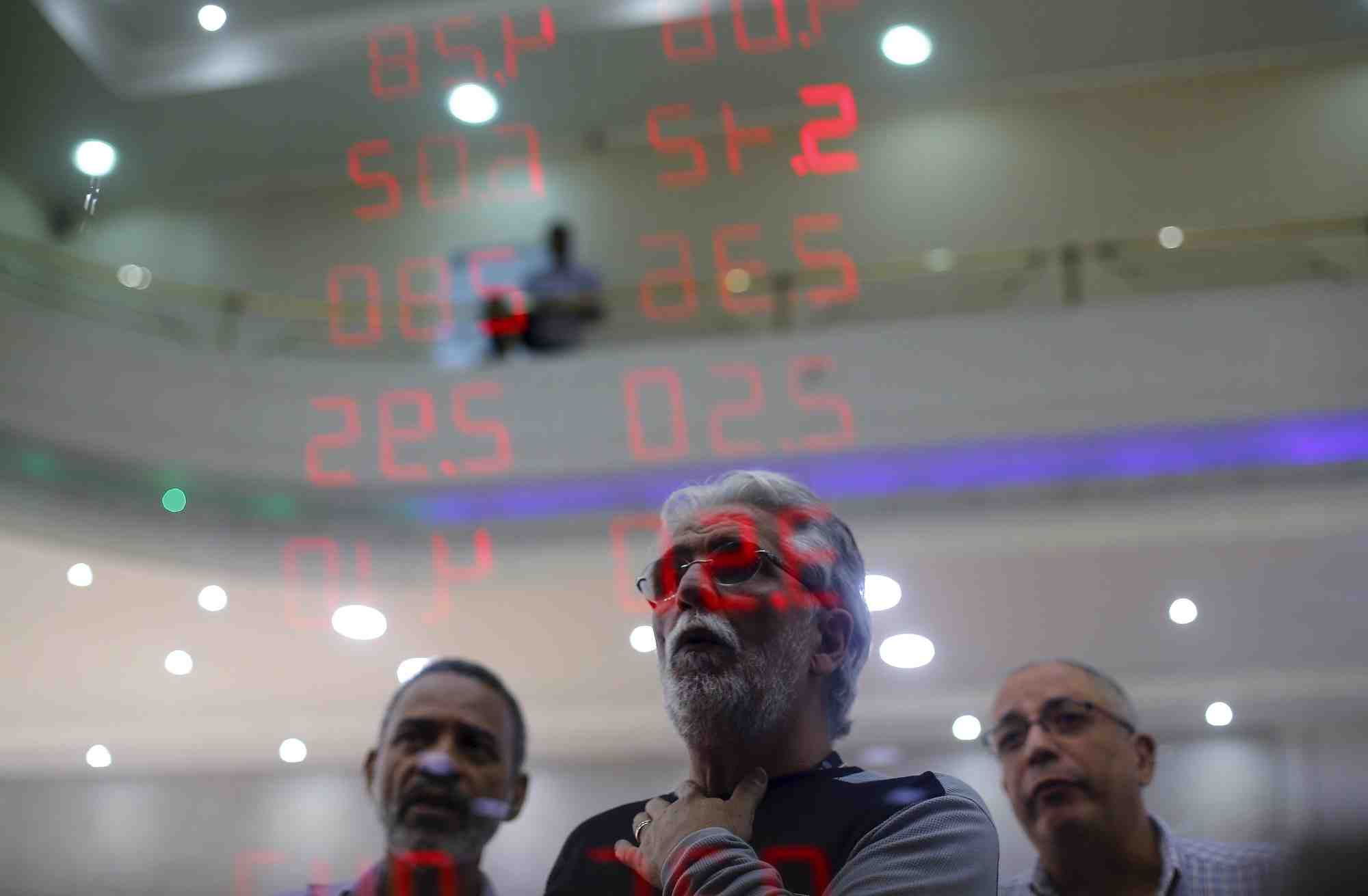 Des hommes reagissent en lisant un tableau affichant les taux de change du real bresilien par rapport au dollar americain et a plusieurs devises etrangeres a rio de janeiro