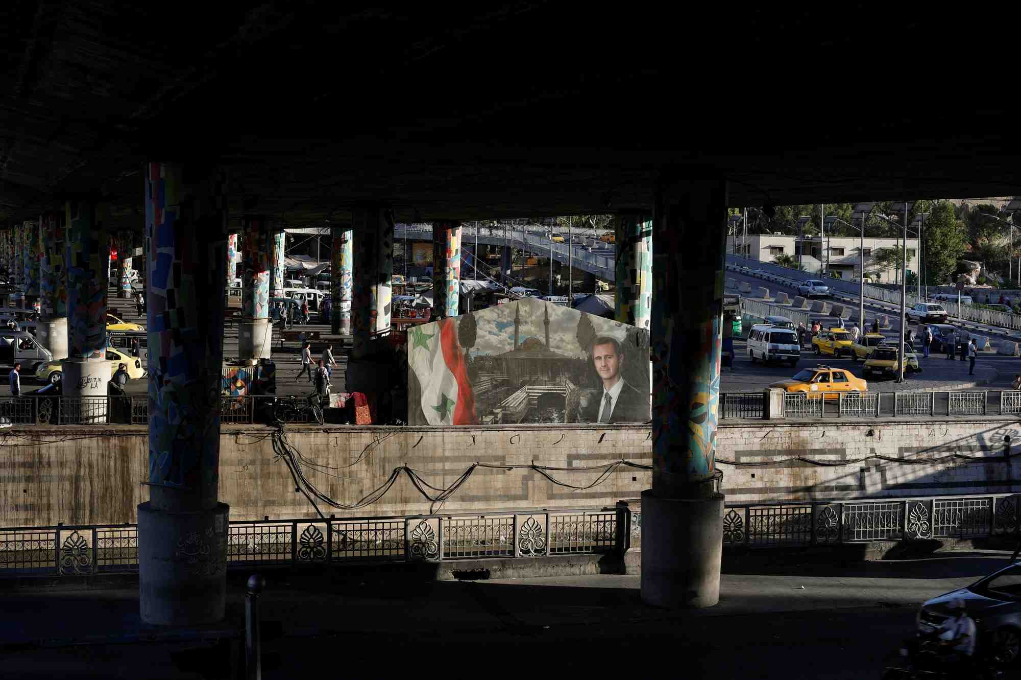 Des taxis circulent pres d'une affiche representant le president syrien bachar al assad, a damas, en syrie