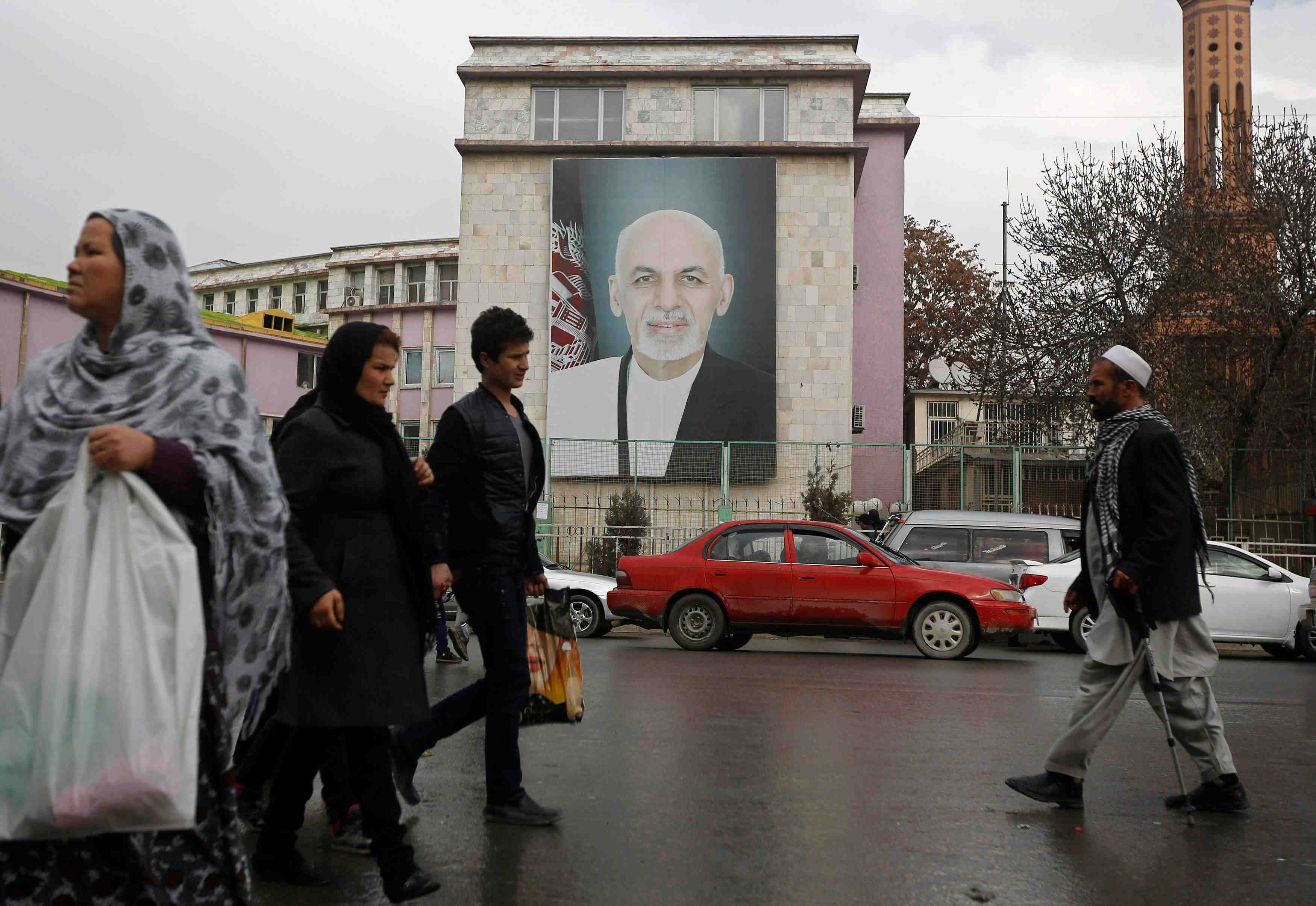 People walk past a picture of afghan president ashraf ghani on a street in kabul