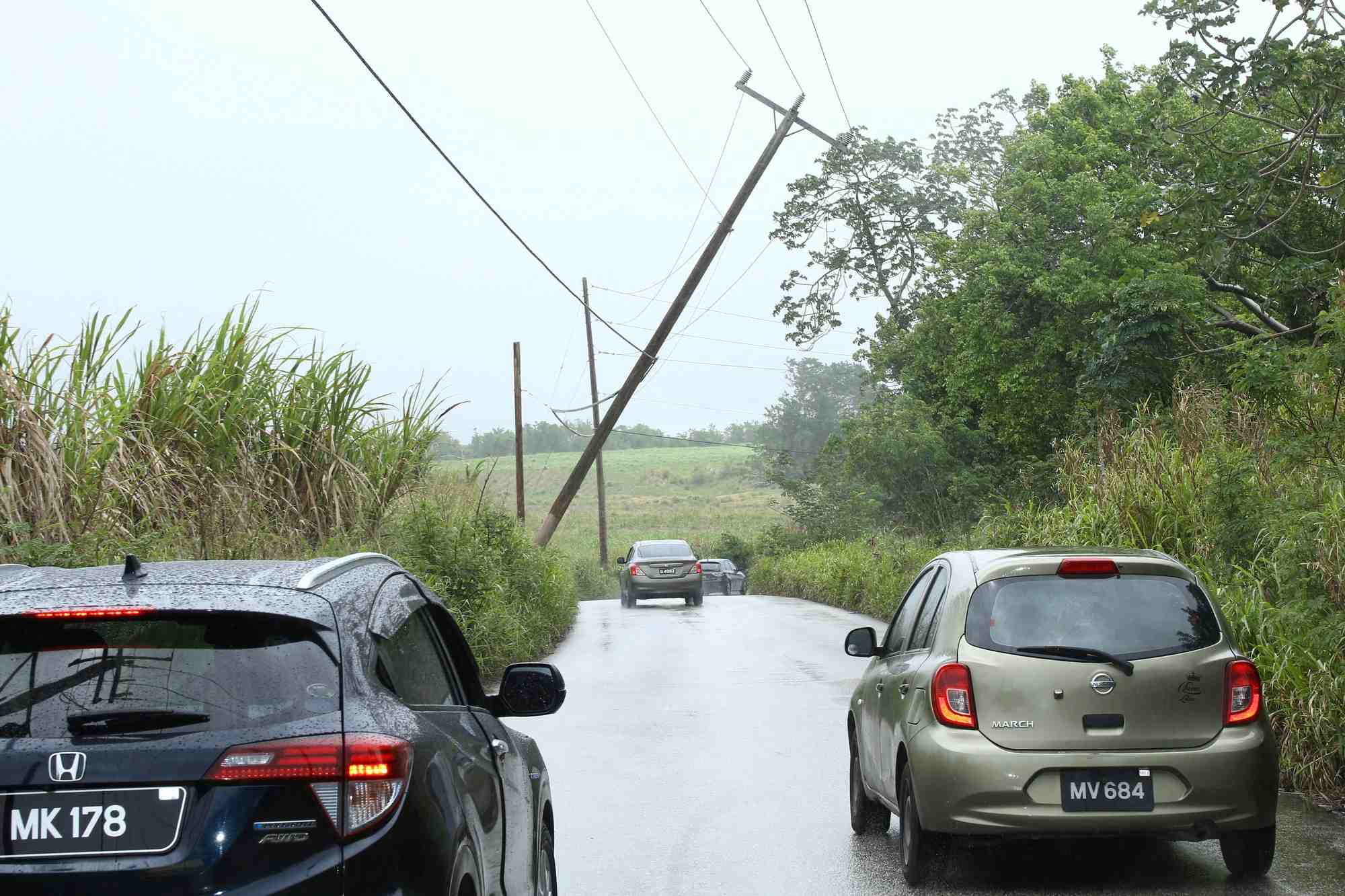 Des voitures passent devant un poteau electrique penche apres le passage de la tempete tropicale bret au nord de l'ile de la barbade