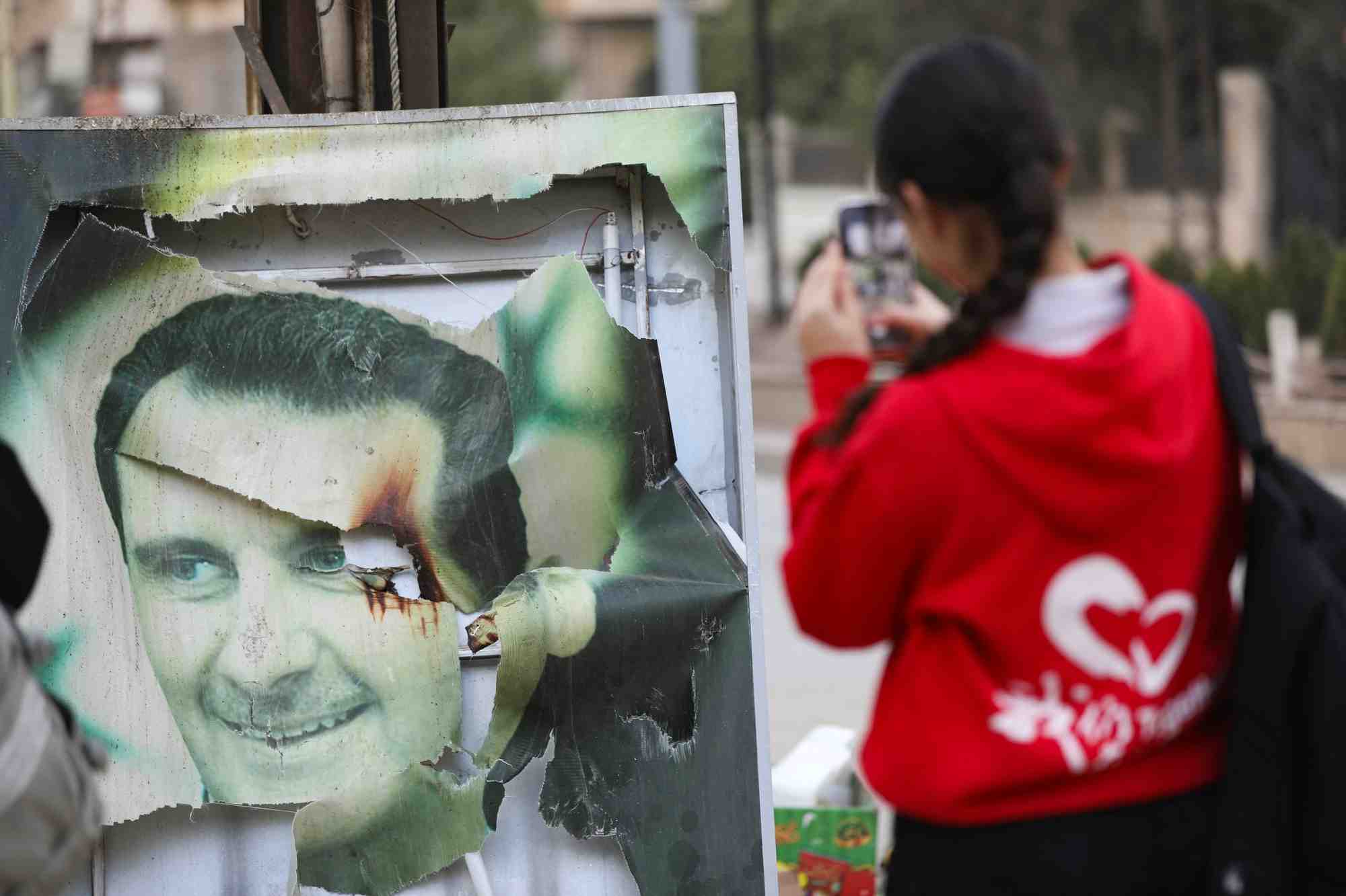 Une femme utilise son telephone portable pres d'une photo endommagee du president syrien bachar al-assad a qamishli, en syrie