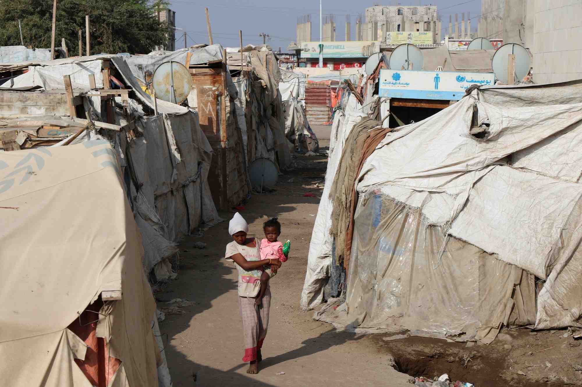 Une fille porte un enfant alors qu'elle marche dans un camp de fortune pour personnes deplacees a aden