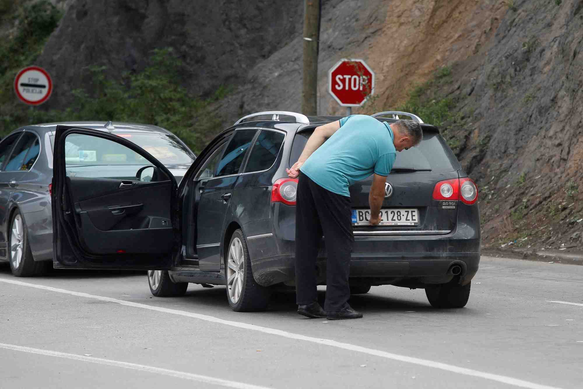 Photo d'archives d'un conducteur retirant un autocollant couvrant les marquages nationaux sur les plaques de sa voiture au poste frontiere de jarinje