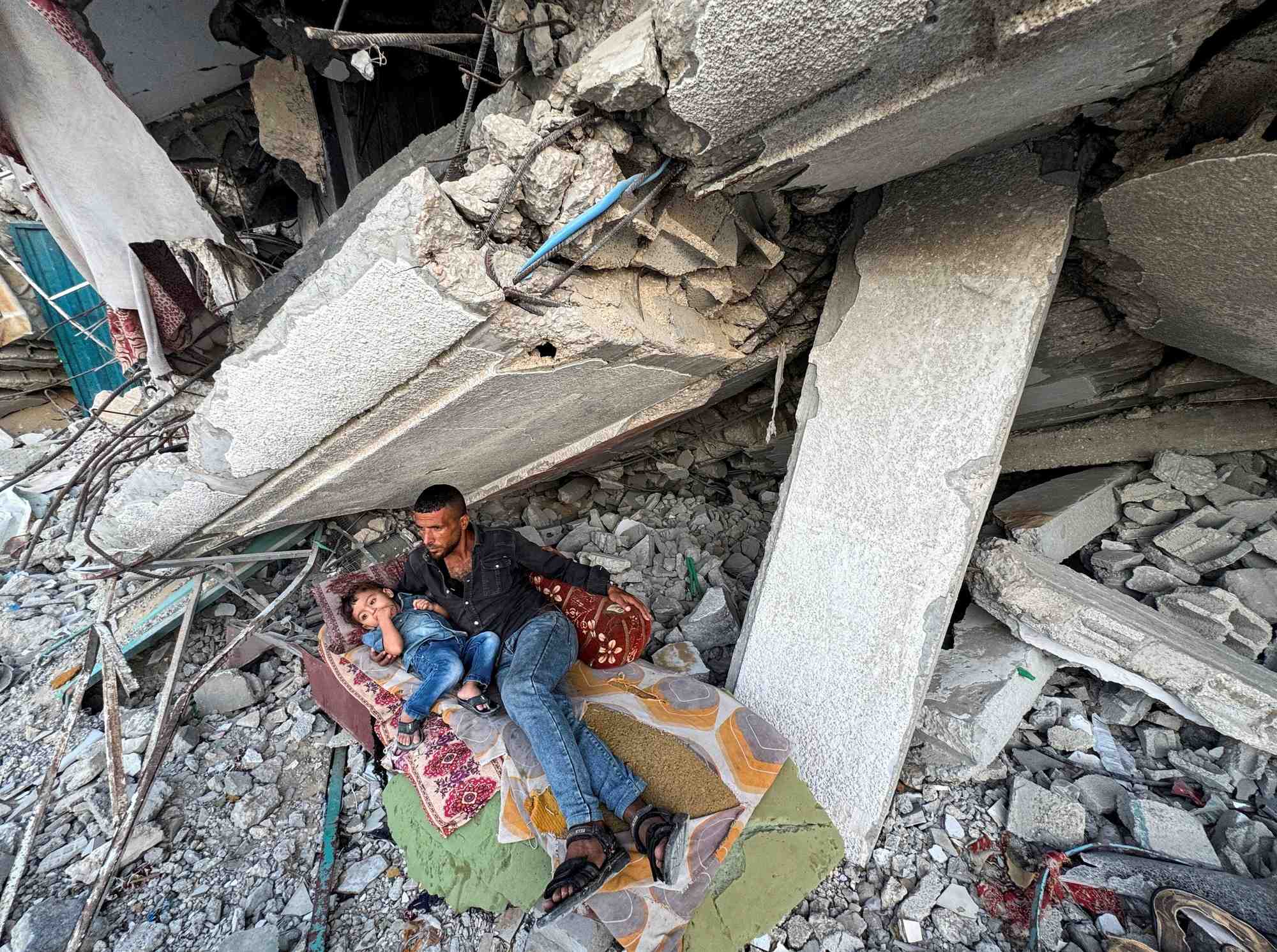 Palestinians rest under the rubble of a house destroyed in israeli strikes, in khan younis
